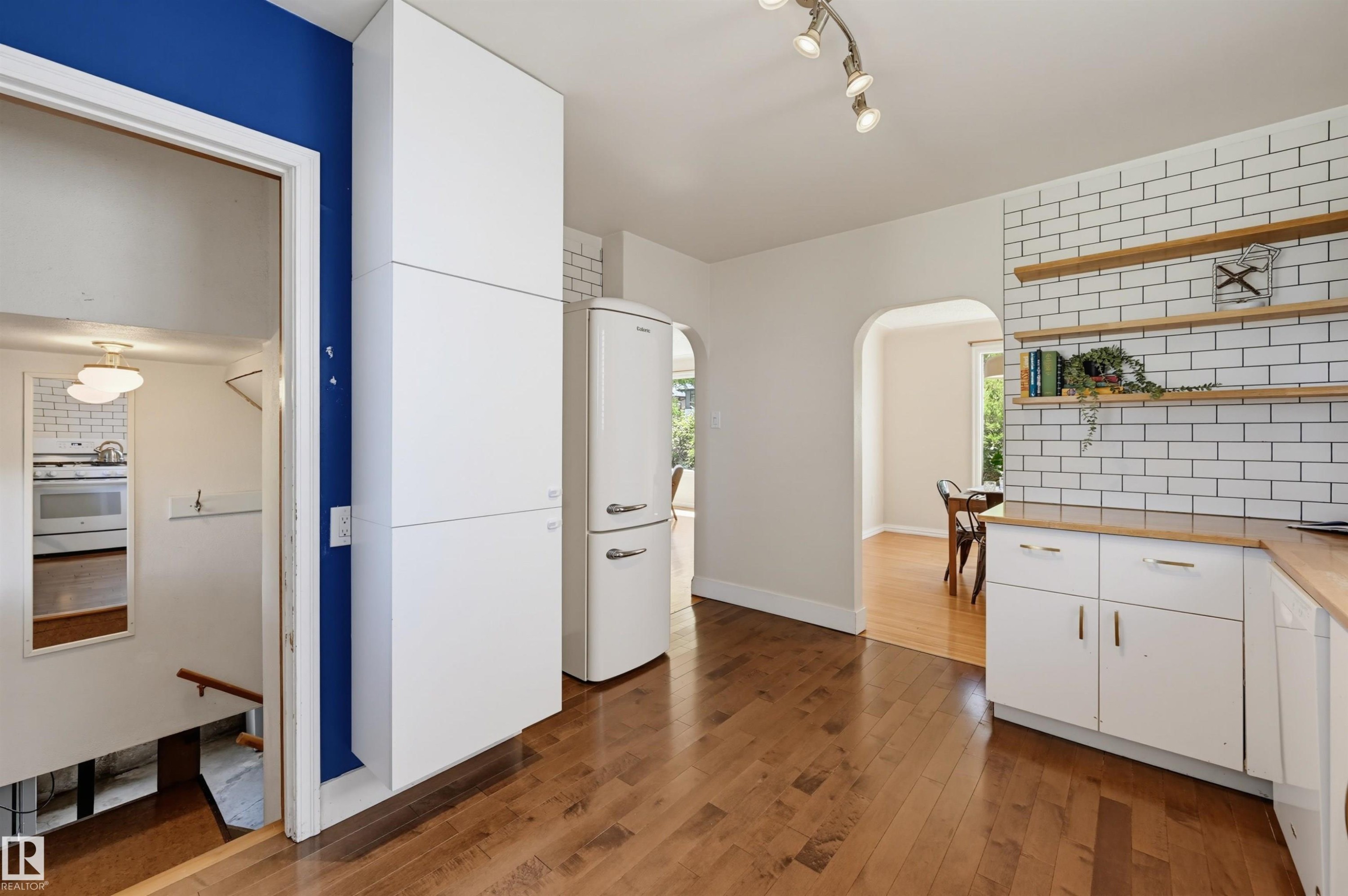 Kitchen featuring wood-finish flooring, white cabinetry with wood countertops, and a white subway tile backsplash with open shelving - 11619 122 Street, Edmonton, AB