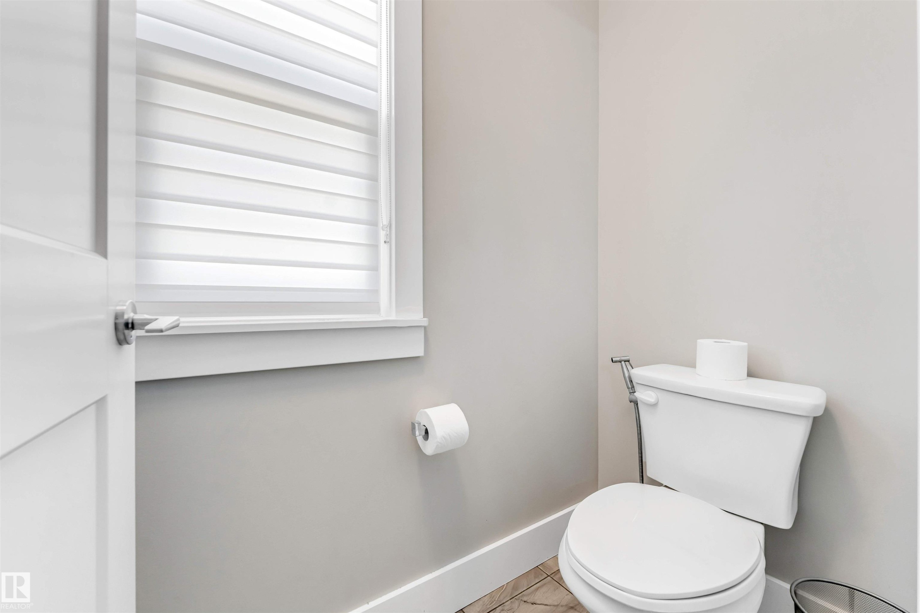 Compact bathroom featuring light gray walls, a white toilet, and a window with horizontal blinds - 8516 216 Street, Edmonton, AB