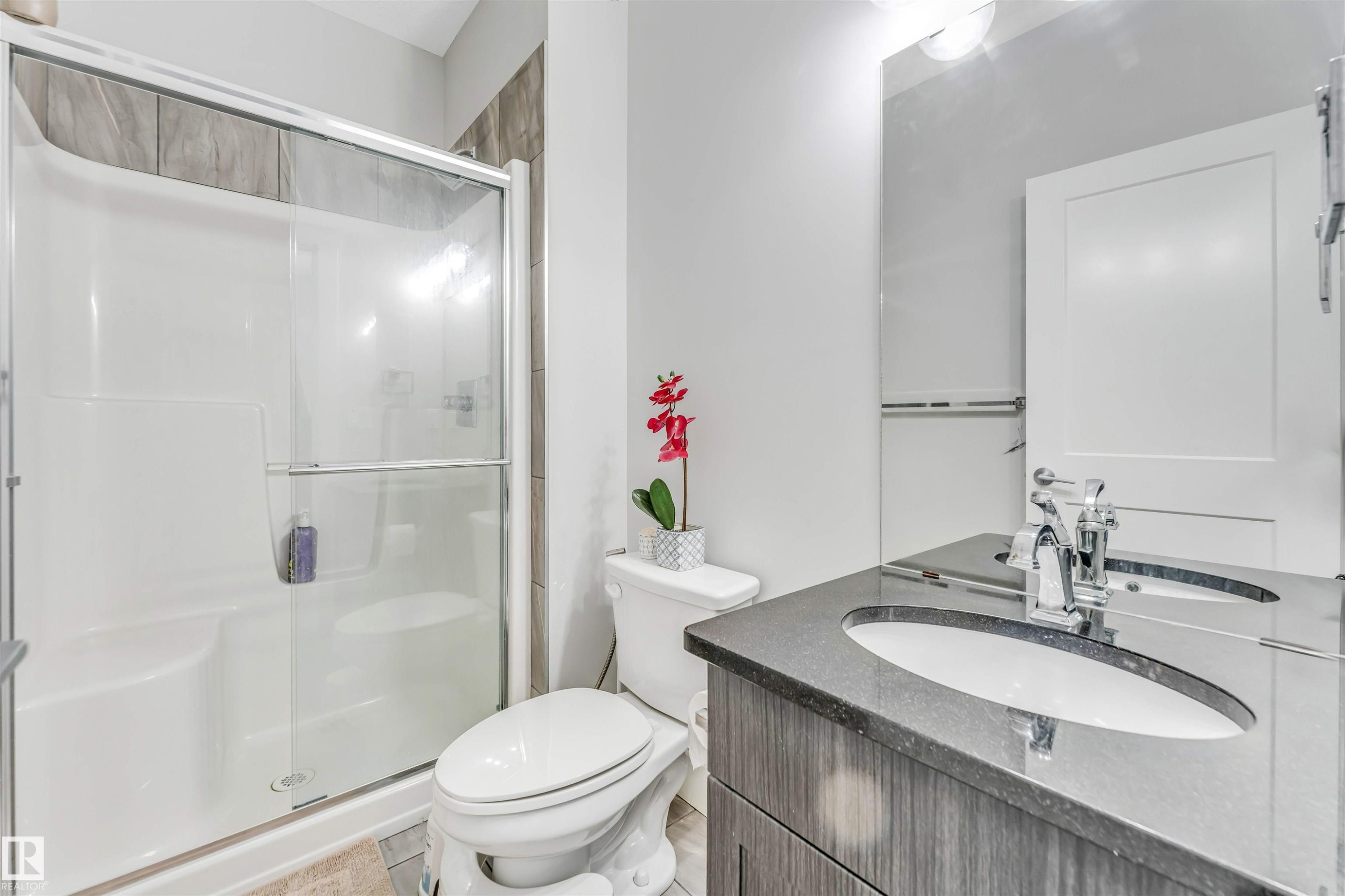 Bathroom featuring a shower stall with sliding glass doors, a vanity with a dark countertop and integrated sink, chrome fixtures, and a white toilet - 8516 216 Street, Edmonton, AB