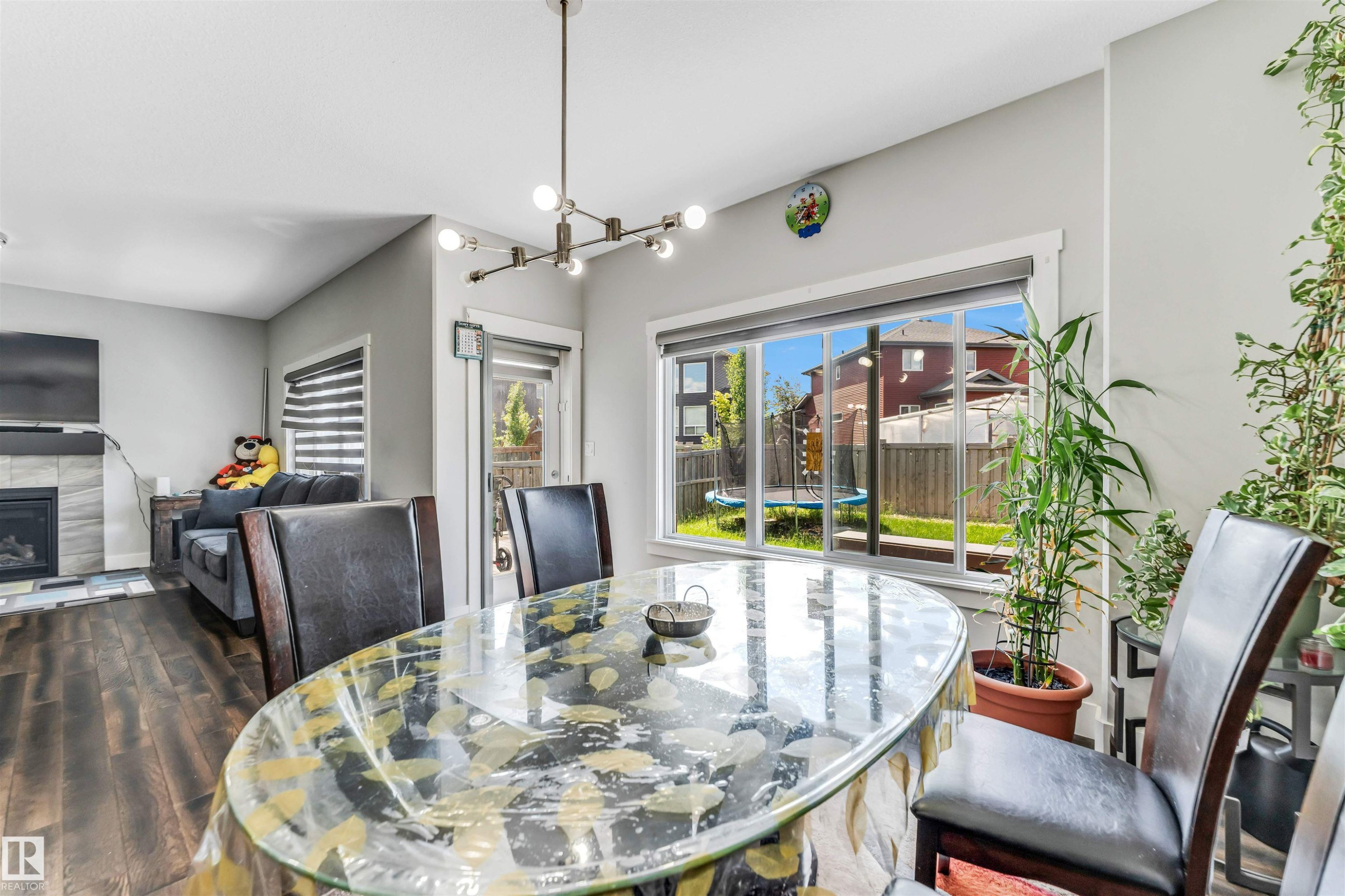 Dining area featuring dark wood-finish flooring, a contemporary linear chandelier, and a large window overlooking the backyard - 8516 216 Street, Edmonton, AB