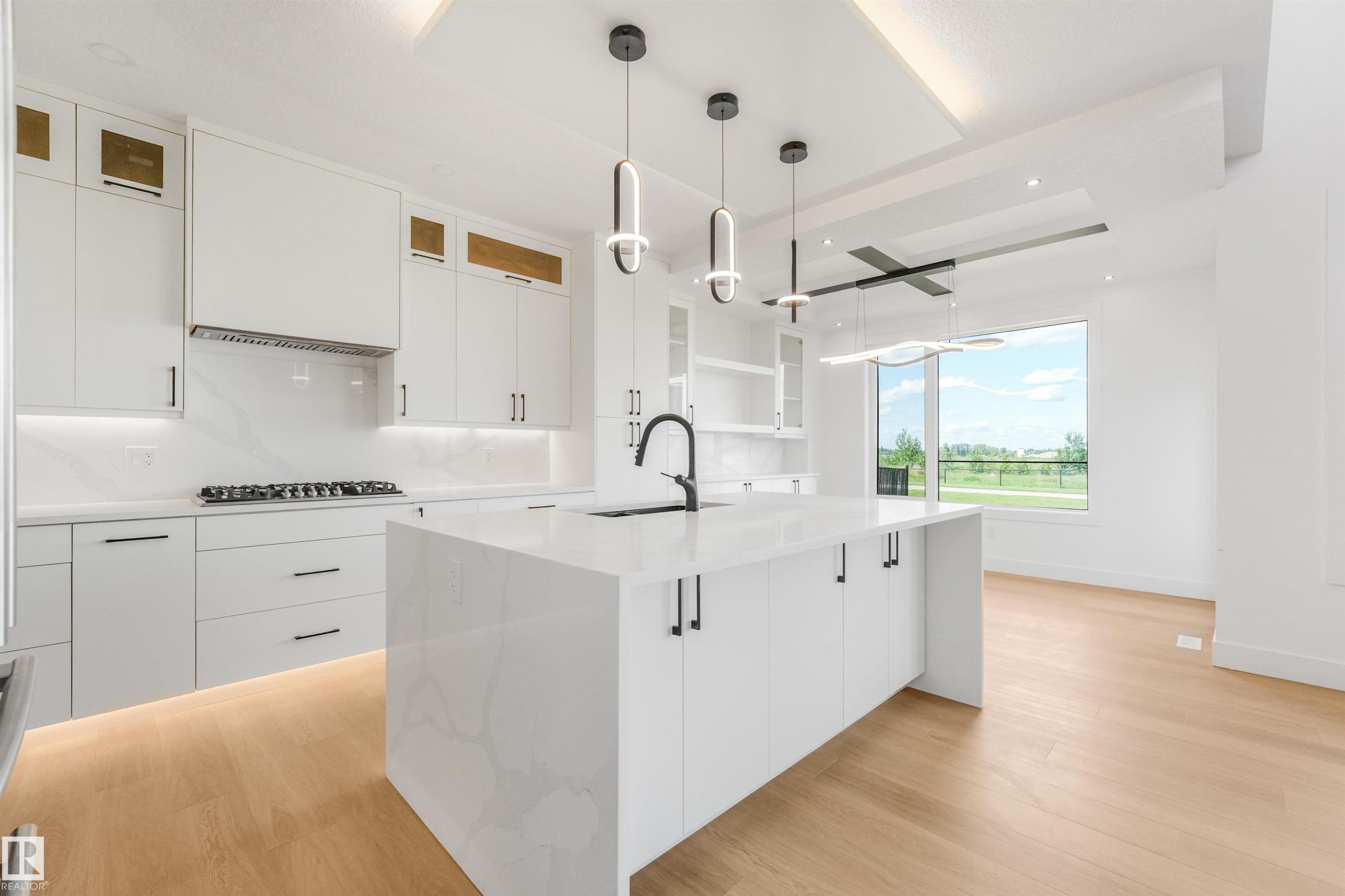 Contemporary kitchen featuring a waterfall island with integrated sink, white cabinetry with dark hardware, gas cooktop, and light wood-finish flooring - 1180 Genesis Lake Boulevard, Stony Plain, AB