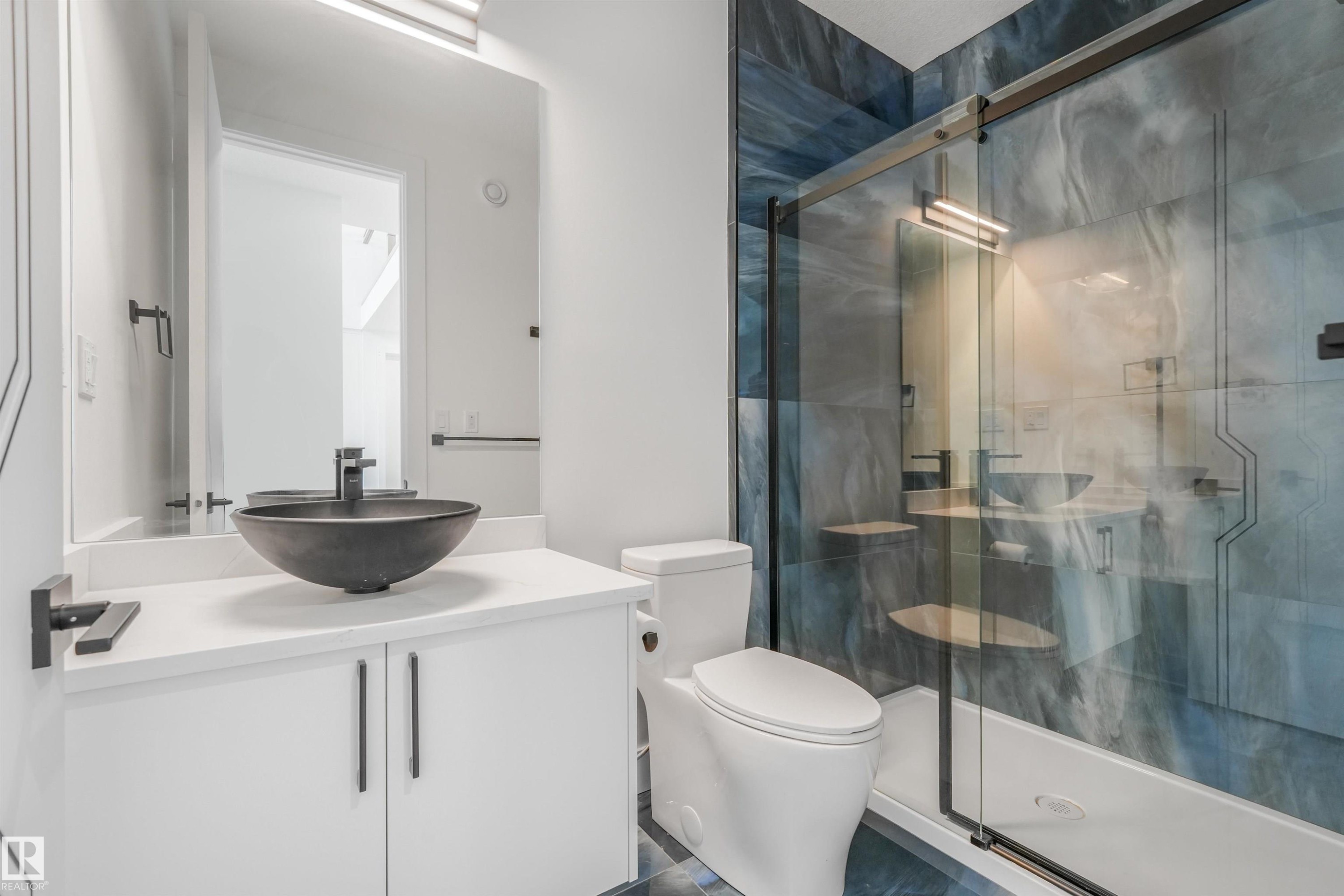 Contemporary bathroom featuring a dark vessel sink, white vanity with matte black hardware, and a glass-enclosed shower with blue-toned tile surround - 1180 Genesis Lake Boulevard, Stony Plain, AB