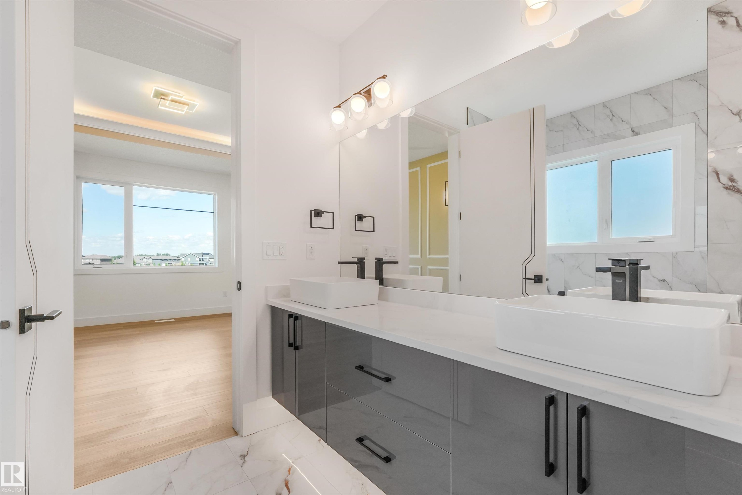 Dual vessel sinks with matte black fixtures, set on a white countertop with a high-gloss gray vanity - 1180 Genesis Lake Boulevard, Stony Plain, AB