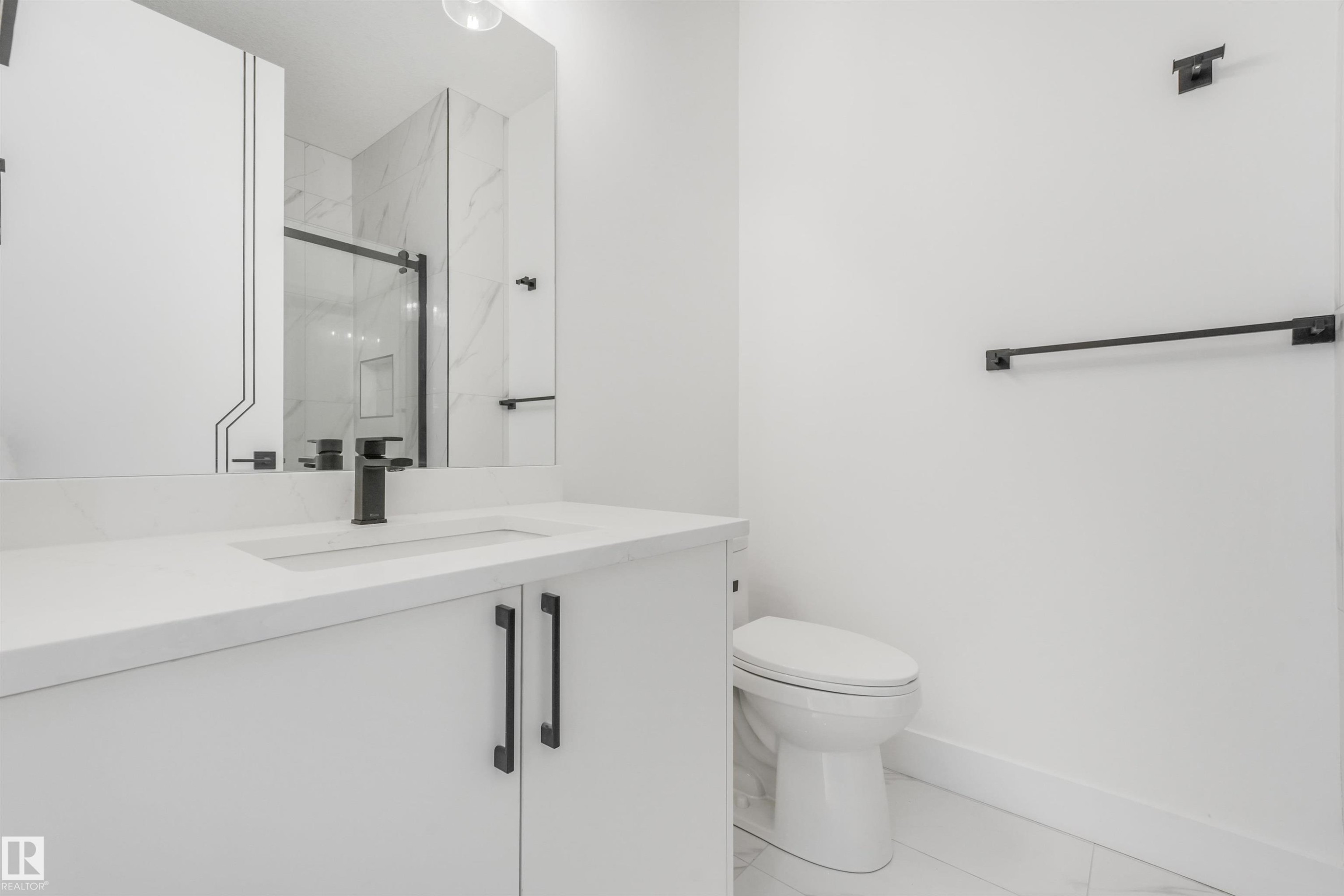 Modern bathroom featuring a white vanity with integrated sink, matte black hardware, and an expansive mirror - 1180 Genesis Lake Boulevard, Stony Plain, AB