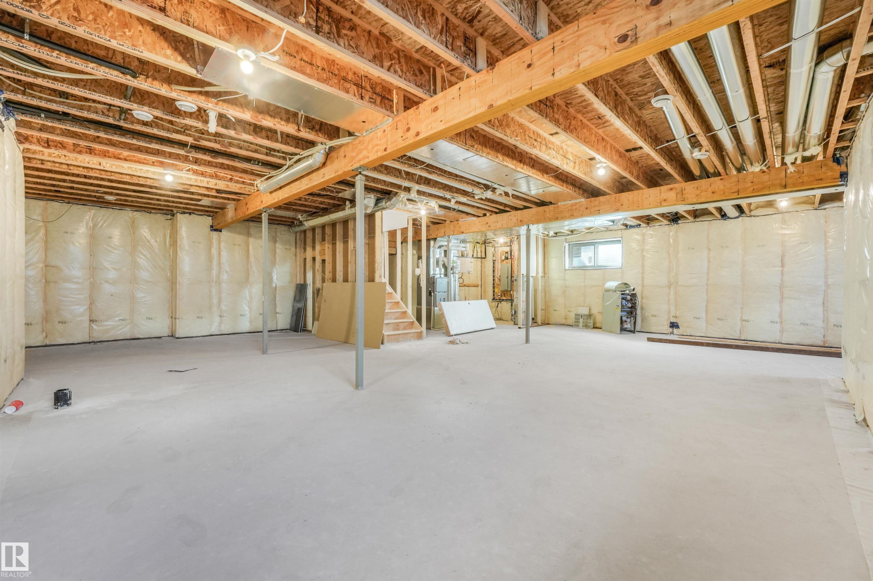 Unfinished basement featuring a concrete floor, exposed wood joists and beams, insulation-backed walls, and a visible window - 1180 Genesis Lake Boulevard, Stony Plain, AB