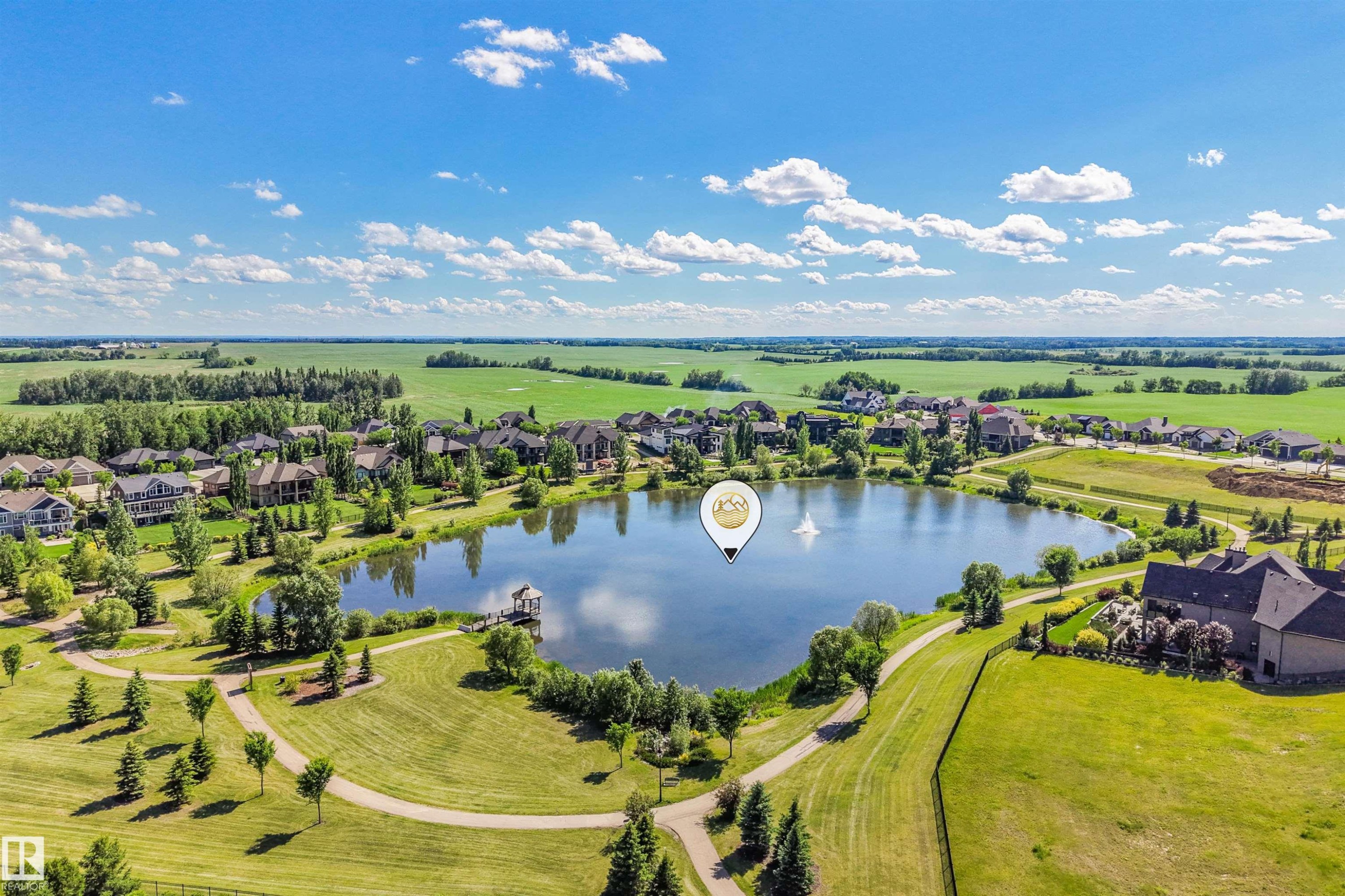 Expansive lakefront setting featuring a central lake, surrounding residential properties, extensive green spaces, and paved walking paths - 1180 Genesis Lake Boulevard, Stony Plain, AB