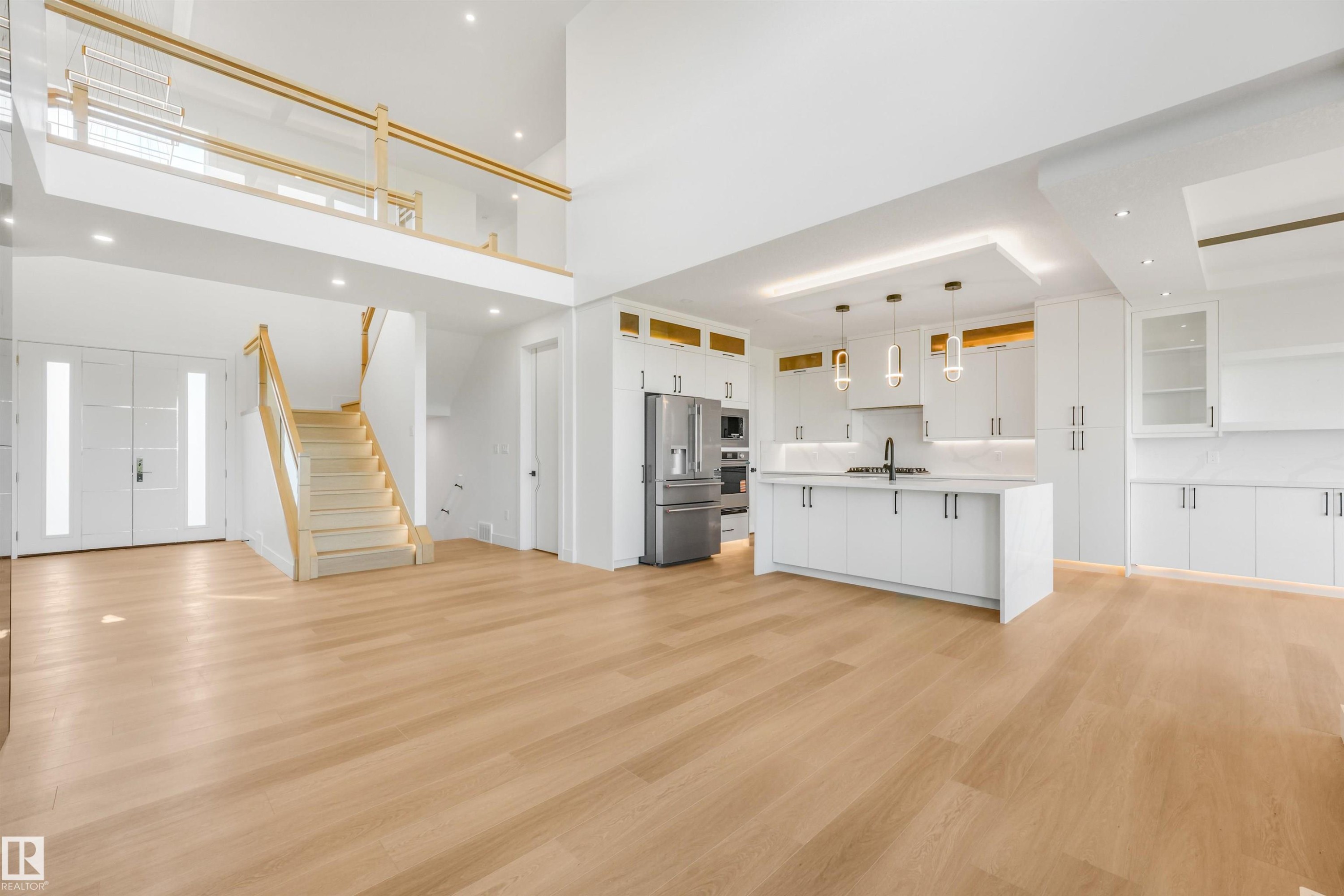 Open-concept living space with light wood-finish flooring, a contemporary kitchen featuring stainless steel appliances and a center island, and a dual-height ceiling - 1180 Genesis Lake Boulevard, Stony Plain, AB
