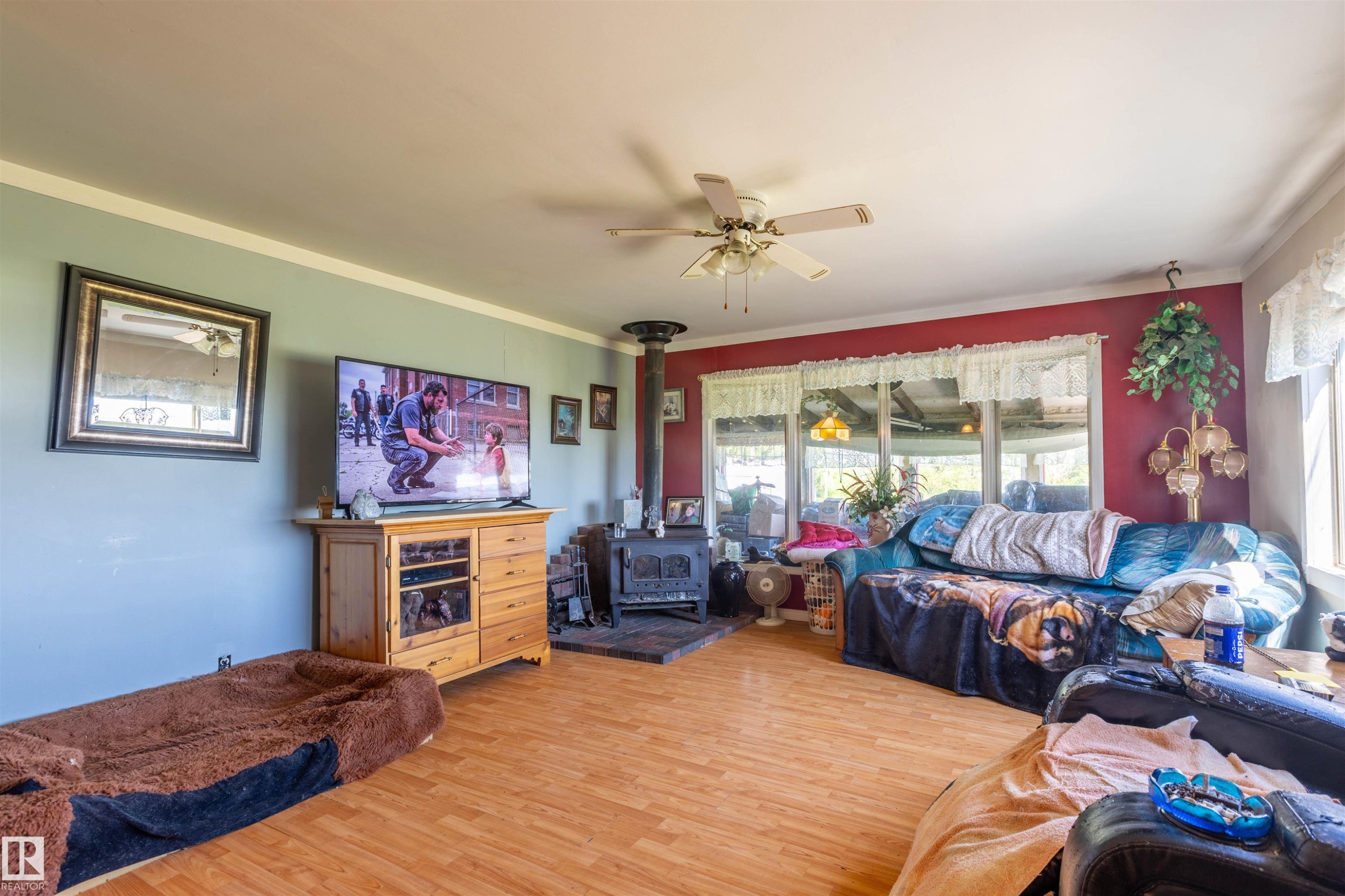 Living area featuring wood-finish flooring, a ceiling fan, and a wood-burning stove with a black pipe - 551027 Range Road 193, Rural Lamont County, AB