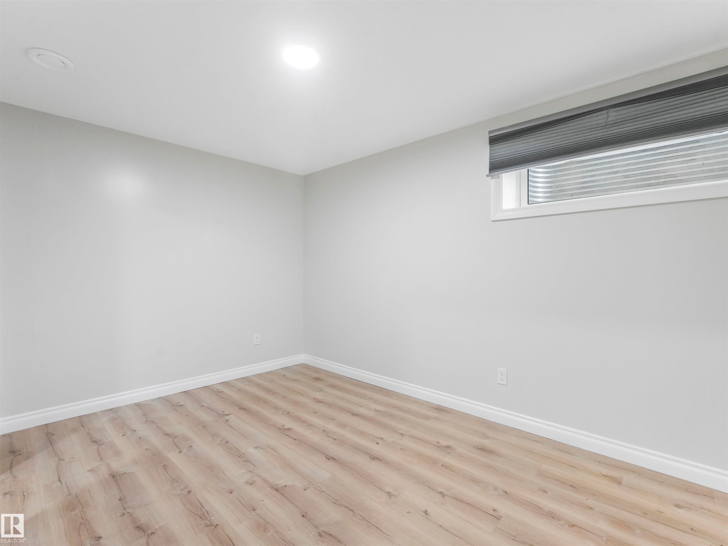 Room with light wood-finish flooring, white baseboards, light gray walls, and a single window with a gray privacy blind - 20507 99 Avenue, Edmonton, AB - Indoor Photo Showing Other Room