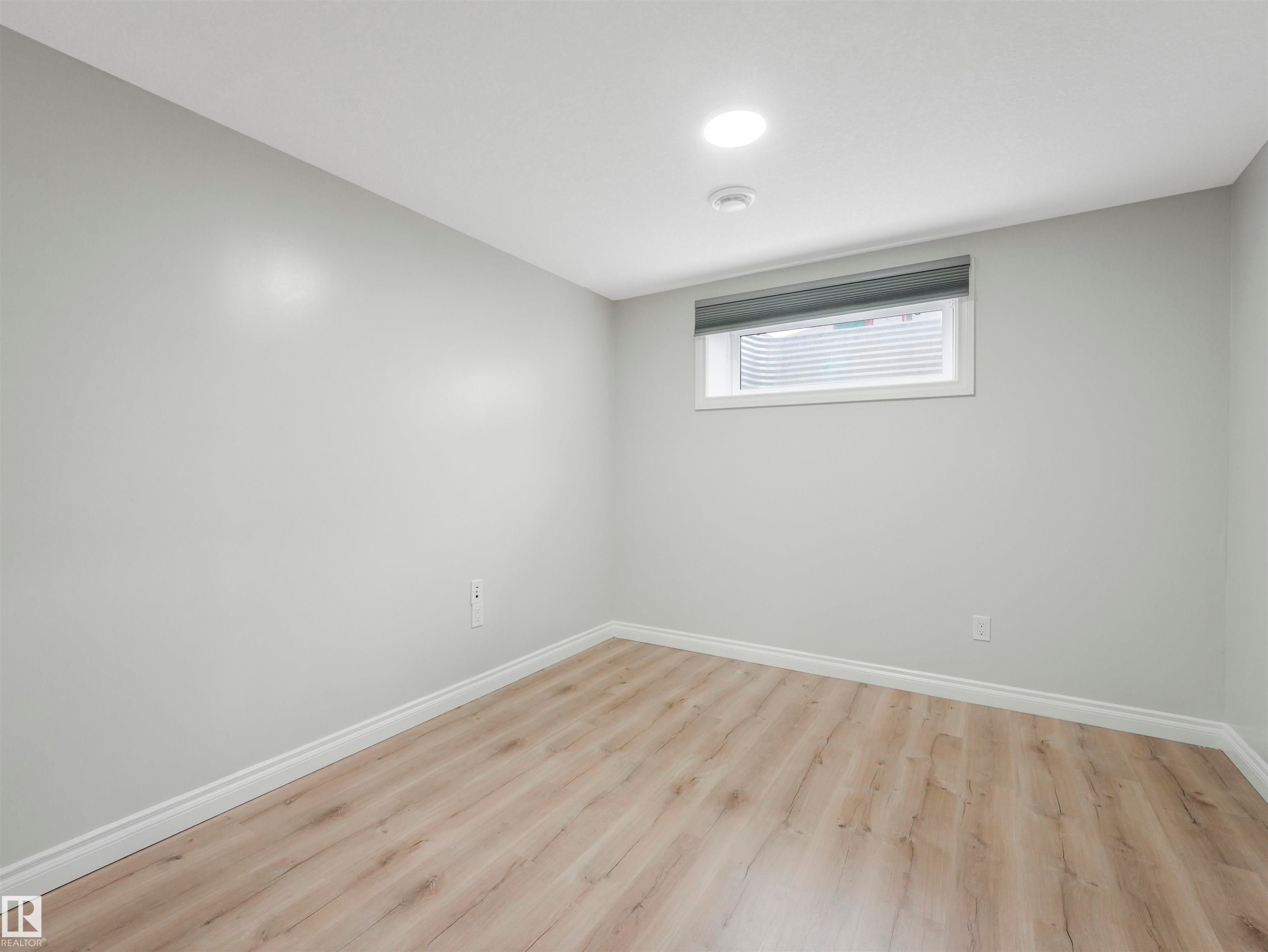 Bright room featuring recessed lighting, a window with a roller shade, light gray walls, white baseboards, and wood-finish flooring - 20507 99 Avenue, Edmonton, AB - Indoor Photo Showing Other Room