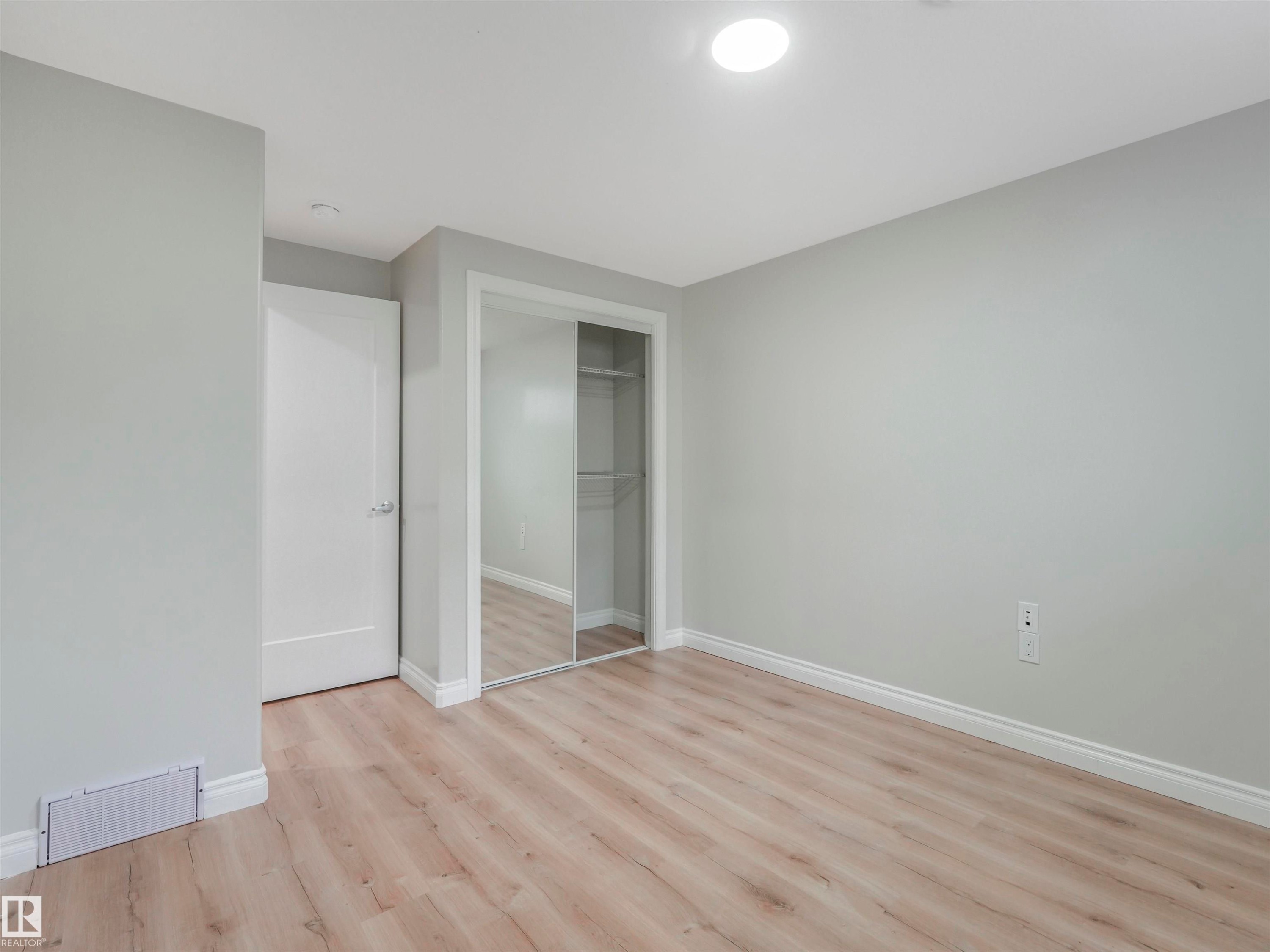 Spacious room featuring light wood-finish flooring, light gray walls, white baseboards, a white interior door, a large mirrored closet, and an overhead recessed light fixture - 20507 99 Avenue, Edmonton, AB - Indoor Photo Showing Other Room