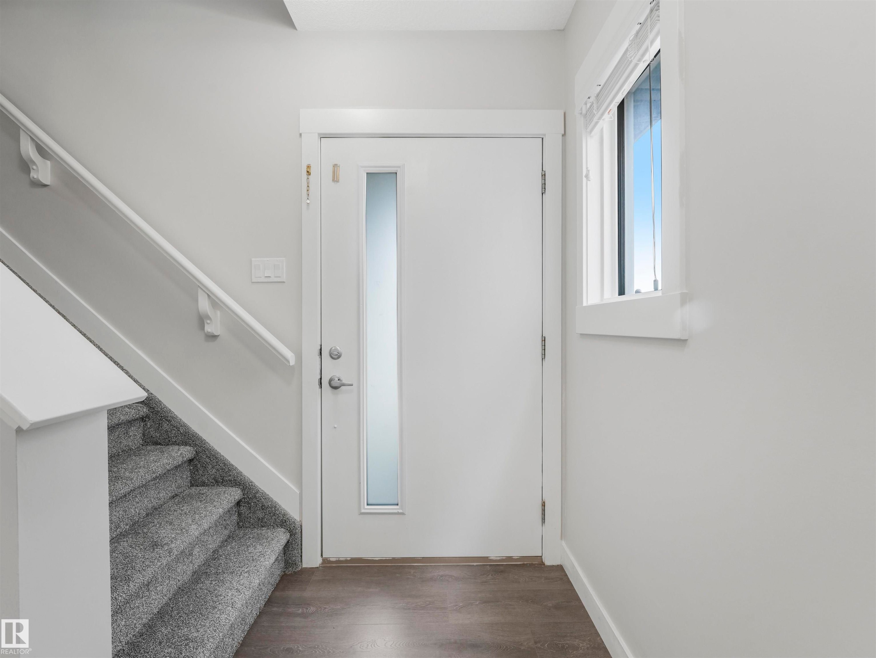 Entryway featuring a white door with a frosted glass insert, wood-finish flooring, a carpeted staircase with white handrail, and a window with white trim - 20507 99 Avenue, Edmonton, AB - Indoor Photo Showing Other Room