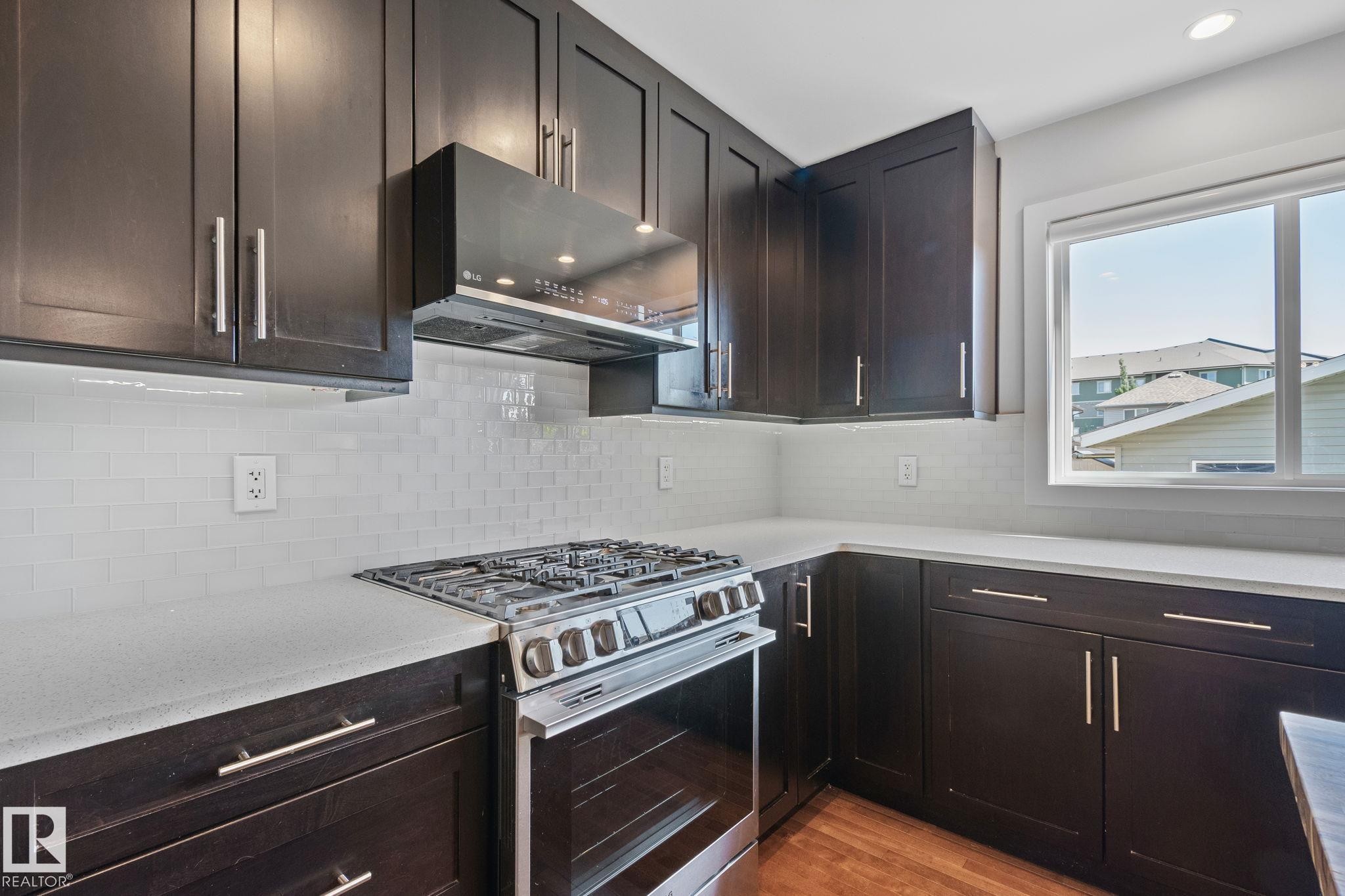 Kitchen featuring dark wood cabinetry, light countertops, a stainless steel range, a subway tile backsplash, and a window - 614 Mcdonough Link, Edmonton, AB