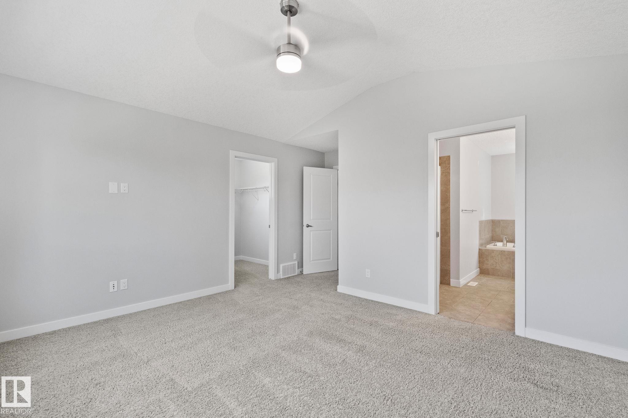 Spacious room featuring light gray carpeting, vaulted ceiling with a modern ceiling fan, and light gray wall paint - 614 Mcdonough Link, Edmonton, AB