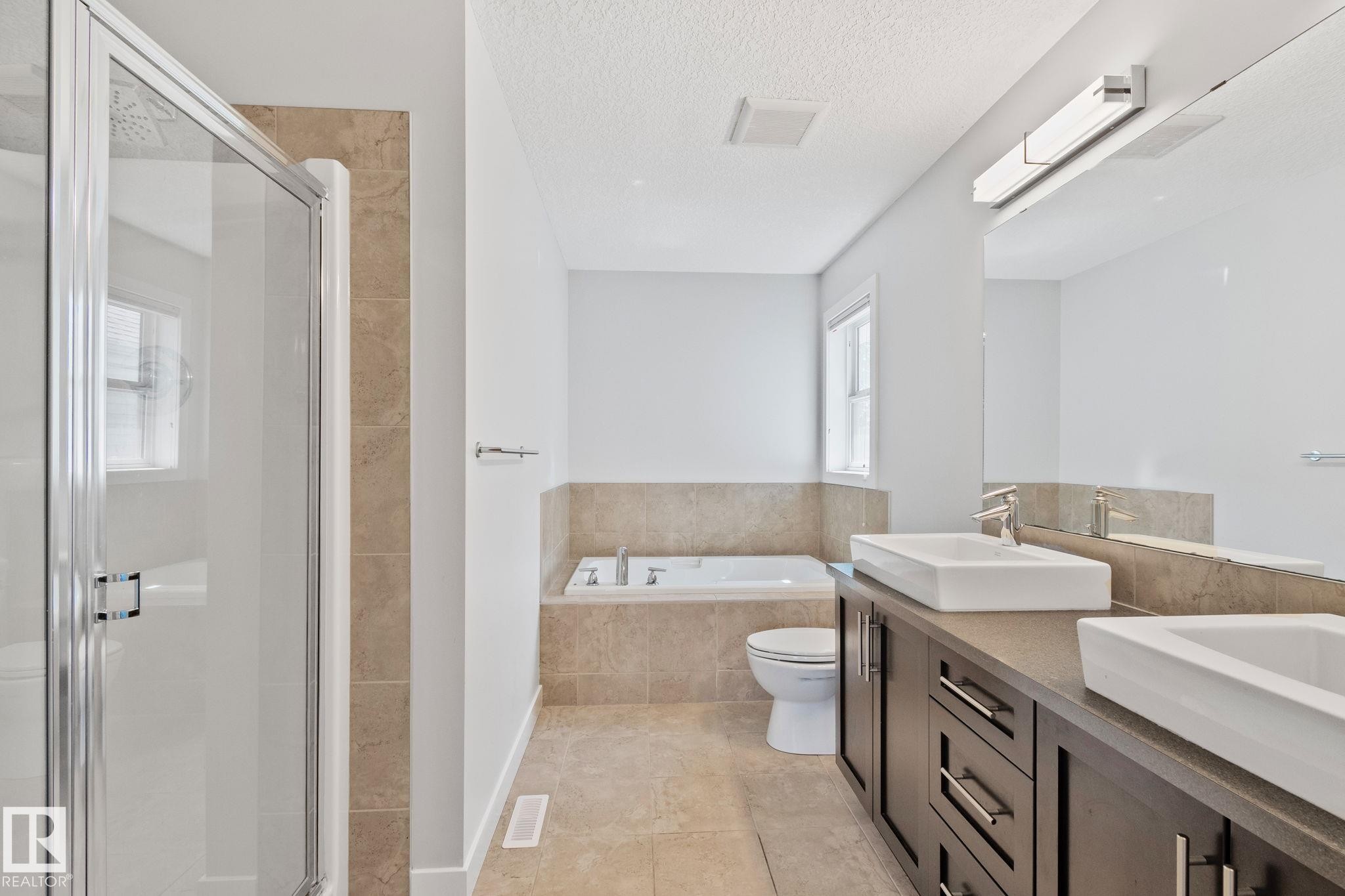 Bathroom featuring a dual vanity with vessel sinks, a walk-in shower with clear glass enclosure, a built-in soaking tub, and tile flooring - 614 Mcdonough Link, Edmonton, AB