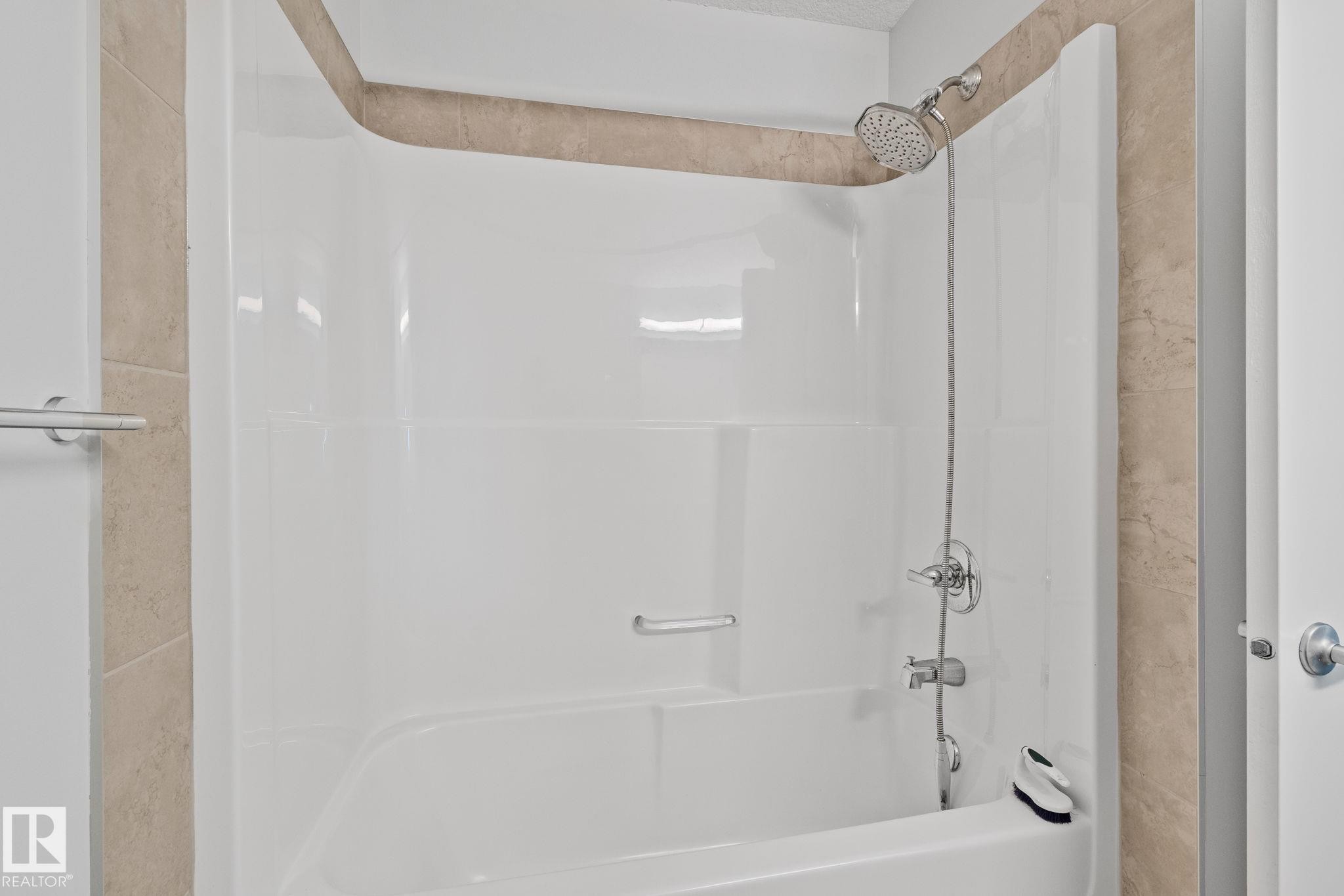 White acrylic tub and shower combination with a handheld shower head, complemented by beige-toned tile surround - 614 Mcdonough Link, Edmonton, AB