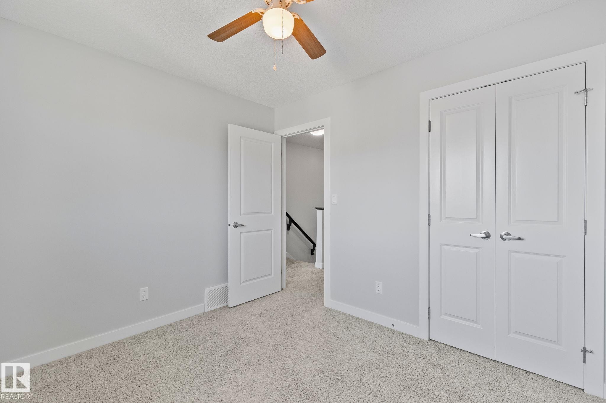 Carpeted room with a ceiling fan light fixture, light gray wall paint, white baseboards, and white paneled doors - 614 Mcdonough Link, Edmonton, AB