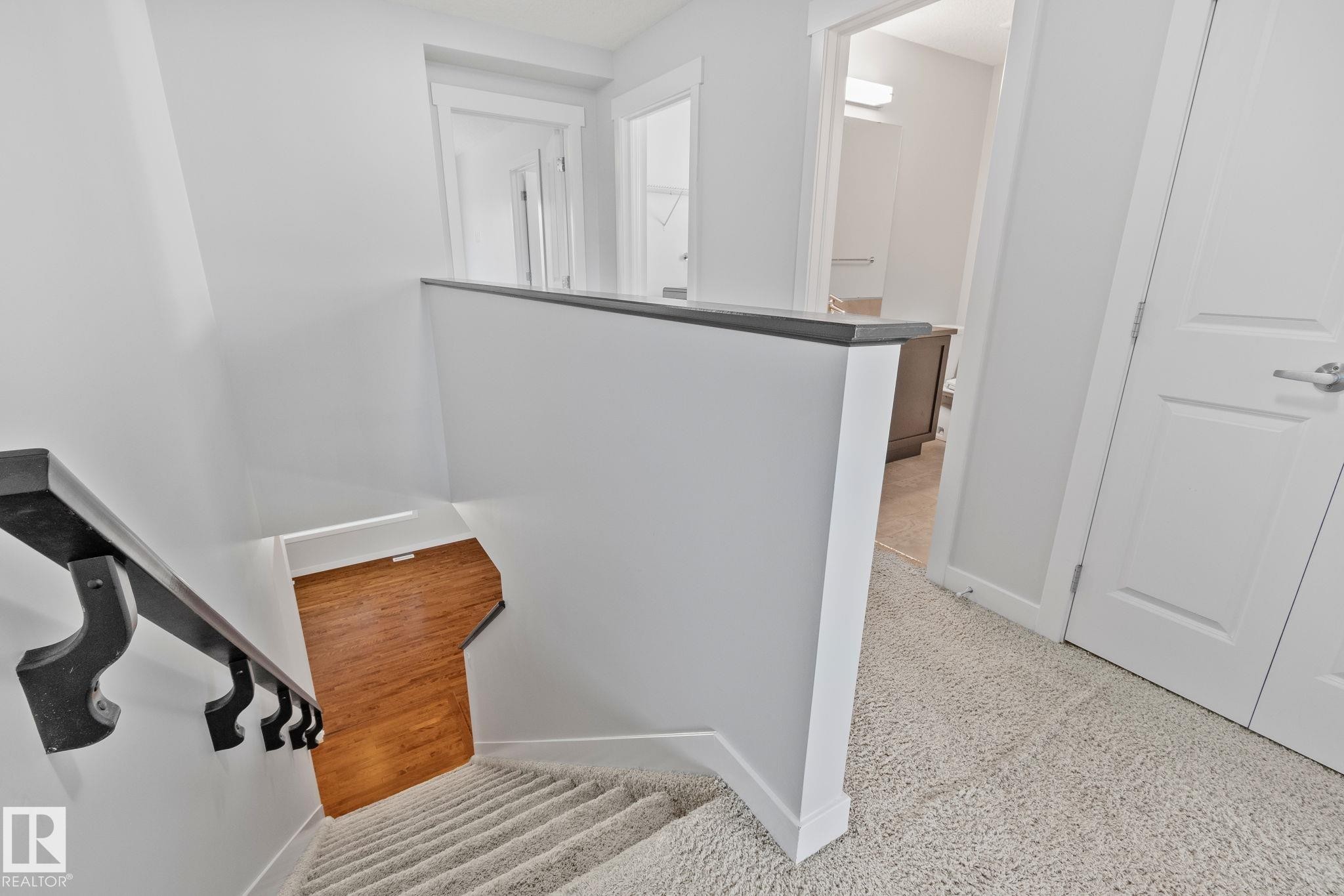 Upper-level landing featuring light-toned carpet, a white banister with a dark wood-finish cap, and solid white doors with brushed nickel hardware - 614 Mcdonough Link, Edmonton, AB
