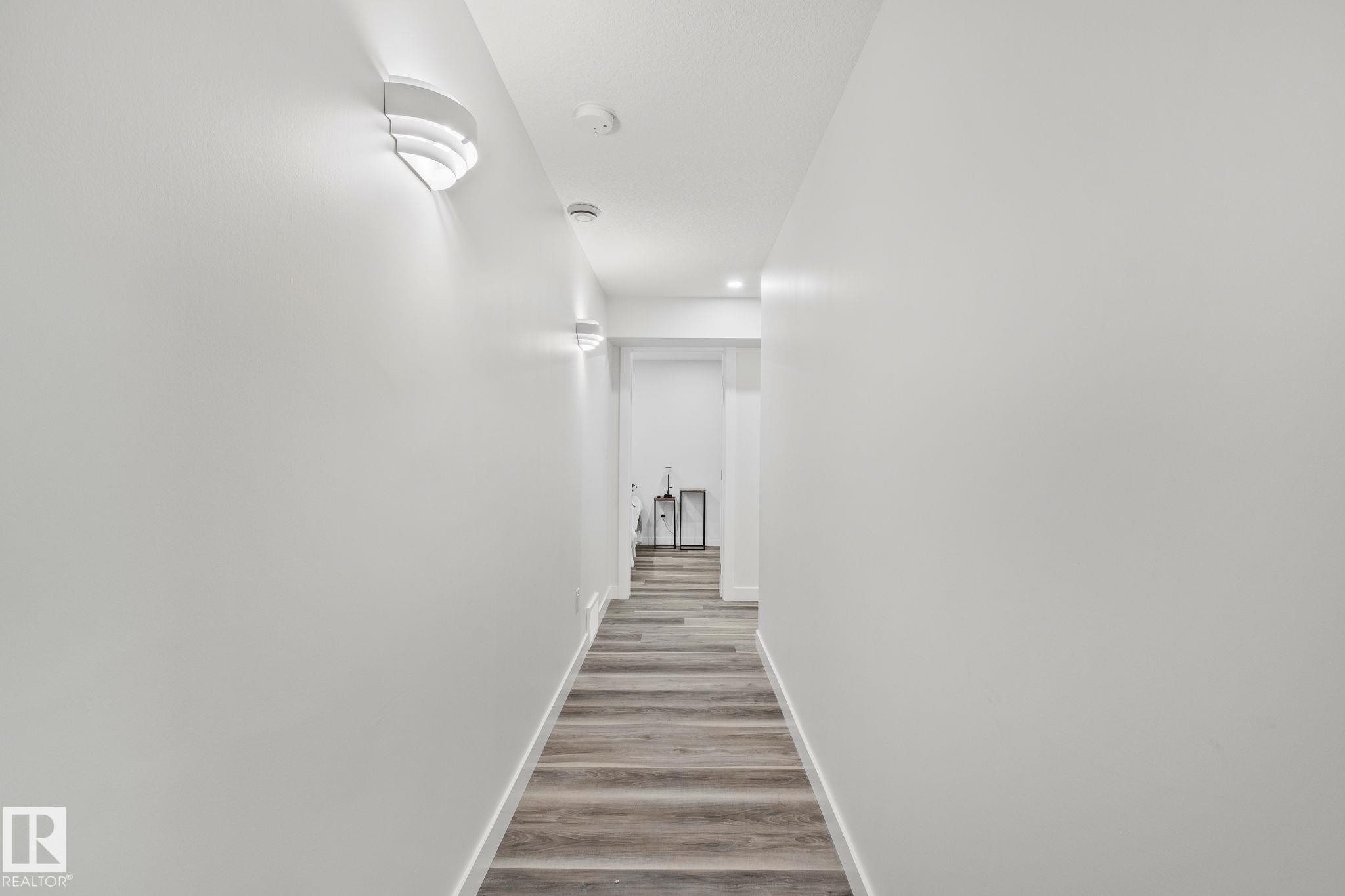 Hallway featuring wood-finish flooring, white baseboards, sconce lighting, and recessed ceiling lights - 614 Mcdonough Link, Edmonton, AB
