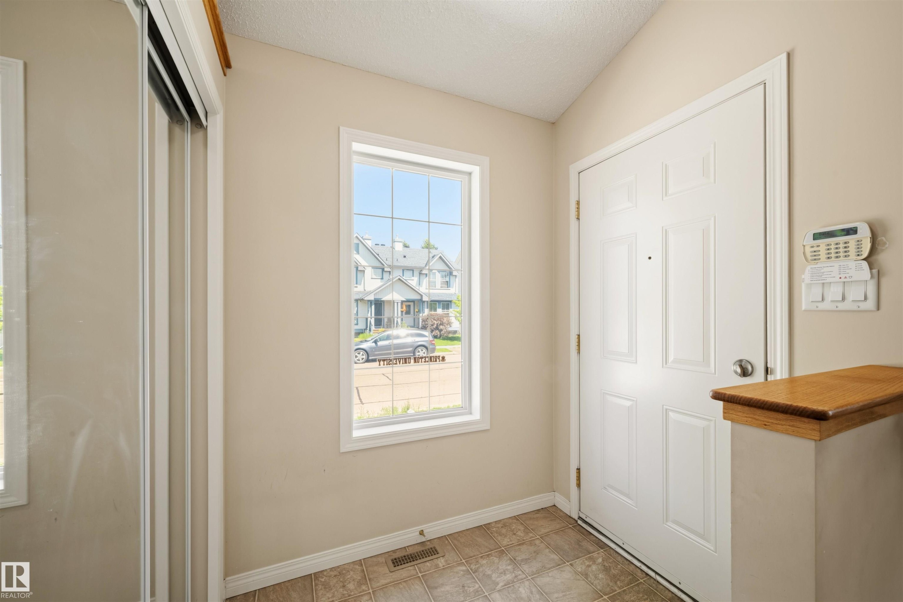 Entry foyer featuring neutral wall tones, durable tile flooring, a multi-pane window, and a built-in security system panel - 7838 Schmid Place Nw, Edmonton, AB - Indoor Photo Showing Other Room