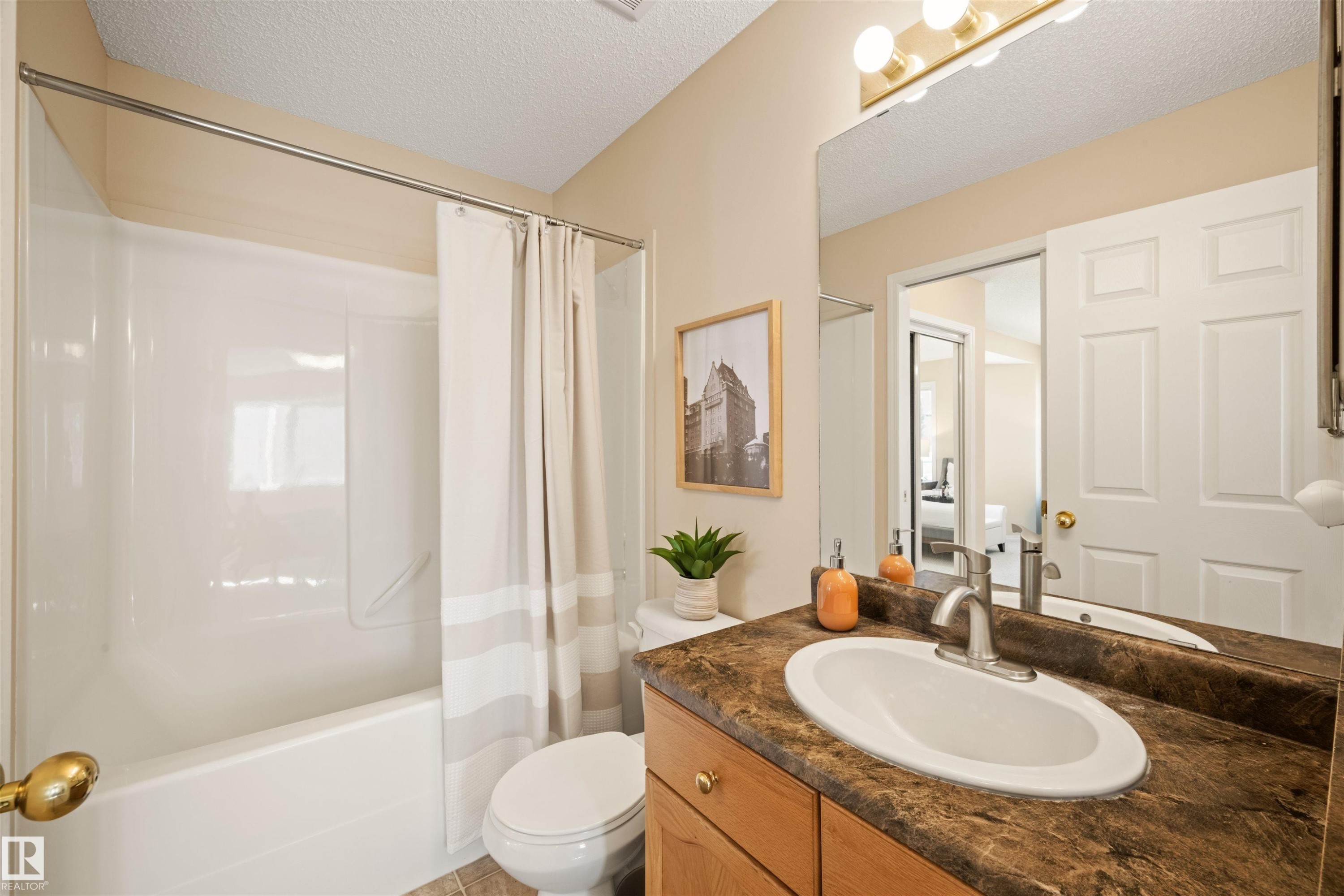 Bathroom featuring a white bathtub with an integrated shower, a white toilet, and a wood-finish vanity with a brown countertop and an integrated sink - 7838 Schmid Place Nw, Edmonton, AB - Indoor Photo Showing Bathroom