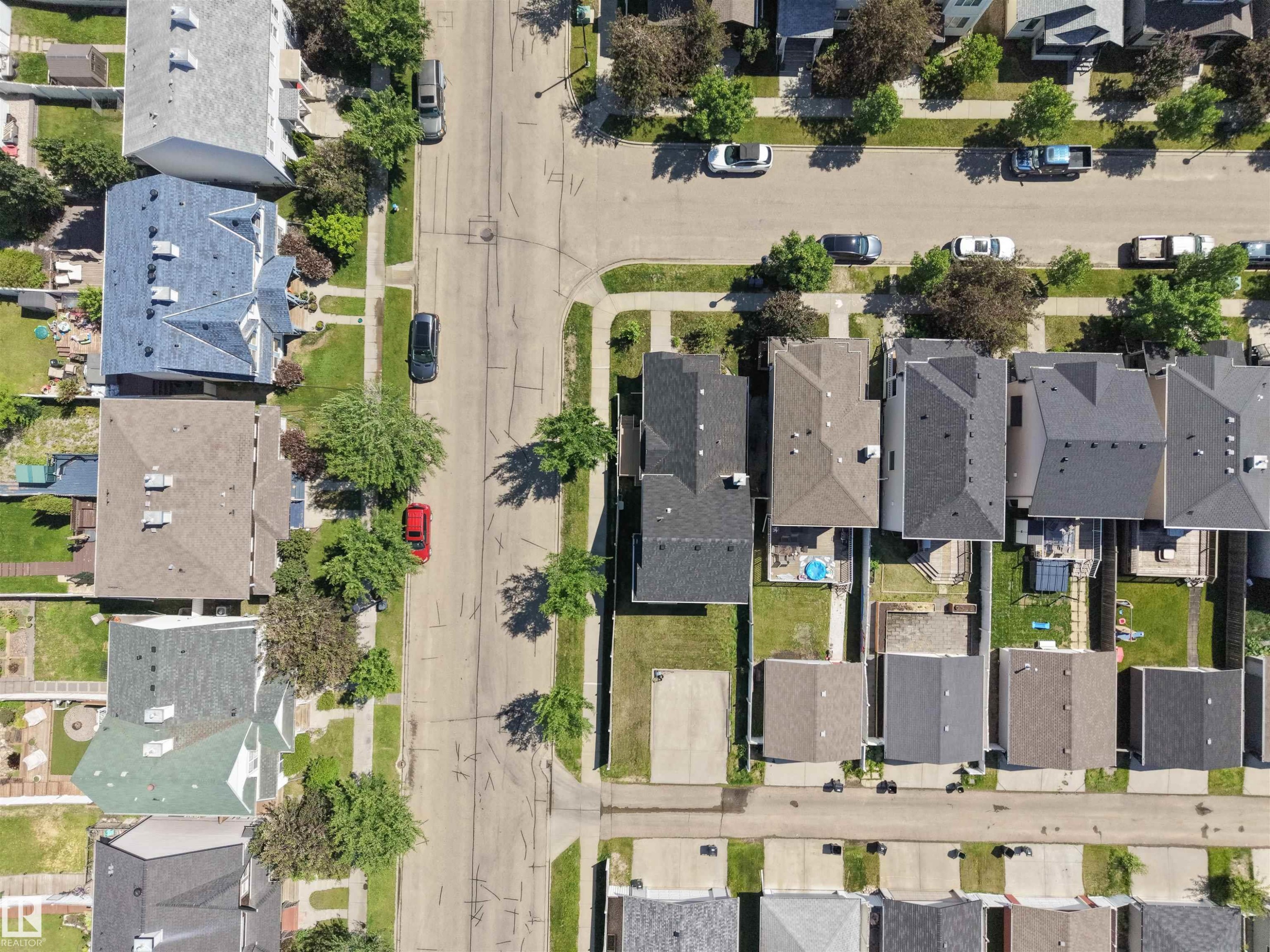 Aerial perspective showcasing a residential street with multiple properties, each featuring varied rooflines, asphalt shingle roofing, and established landscaping including mature trees and green lawns - 7838 Schmid Place Nw, Edmonton, AB - Outdoor With View