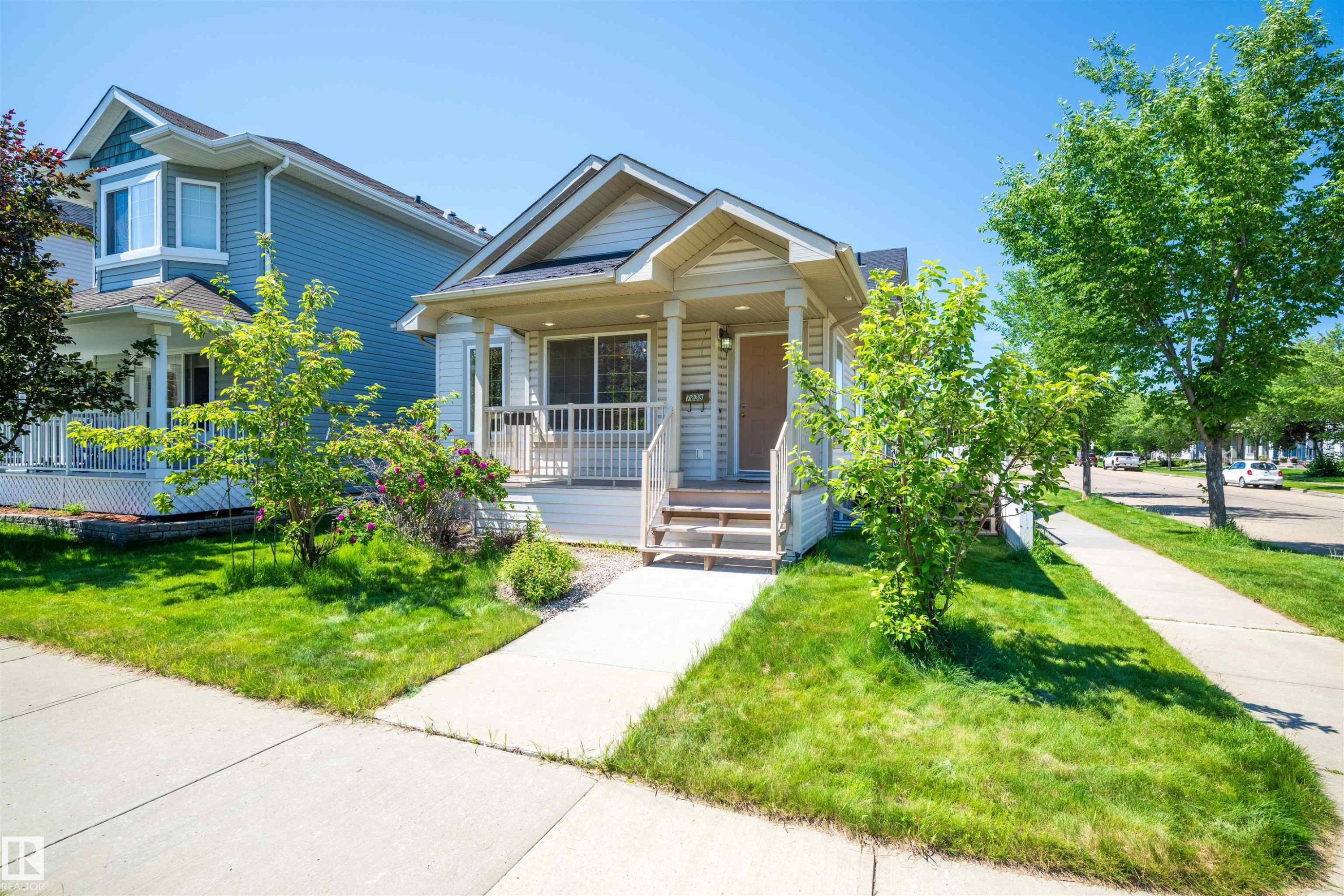 Cream-colored siding home featuring a covered front porch with white railings and columns - 7838 Schmid Place Nw, Edmonton, AB - Outdoor With Facade