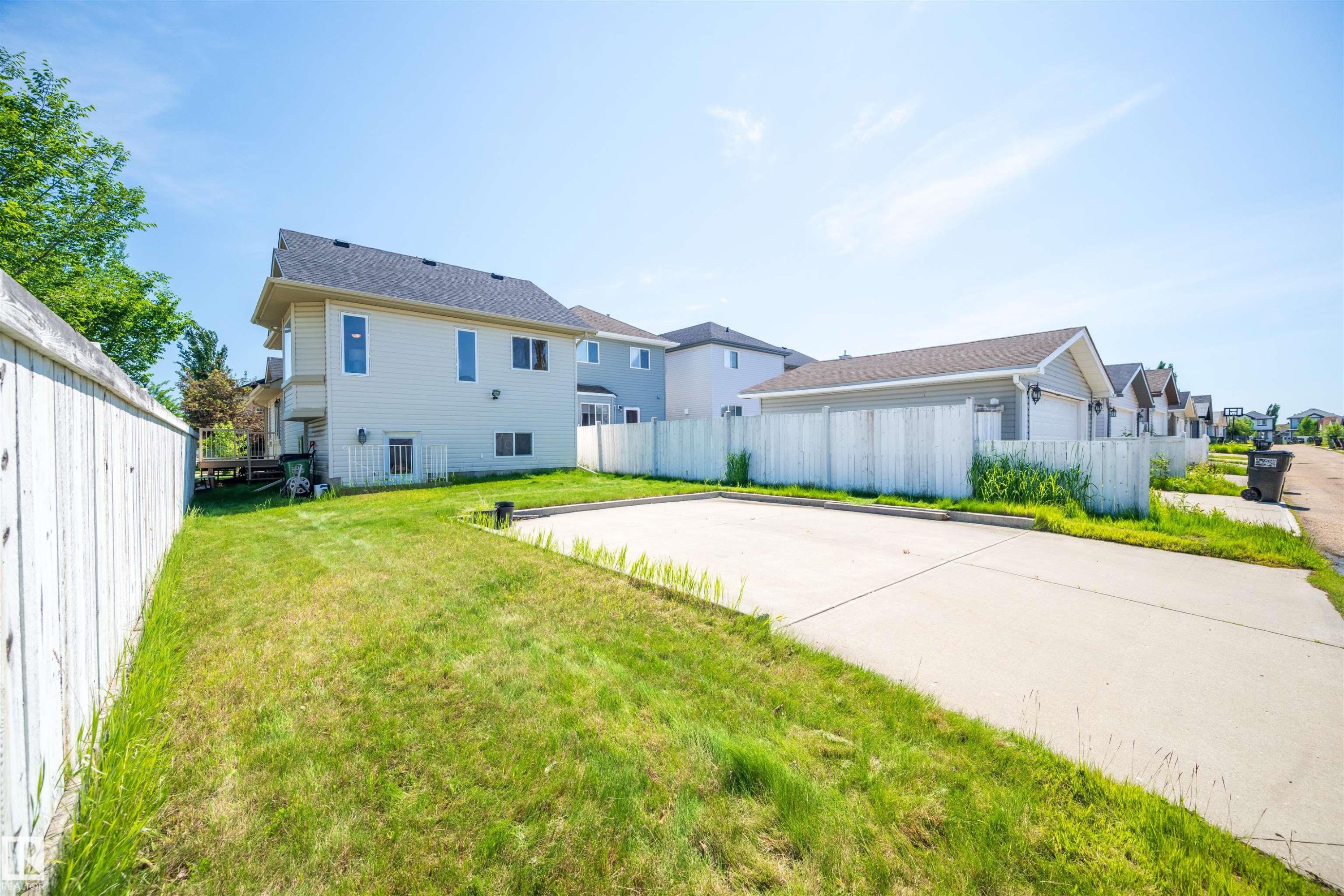 Expansive paved surface with ample grass border, featuring a white privacy fence - 7838 Schmid Place Nw, Edmonton, AB - Outdoor