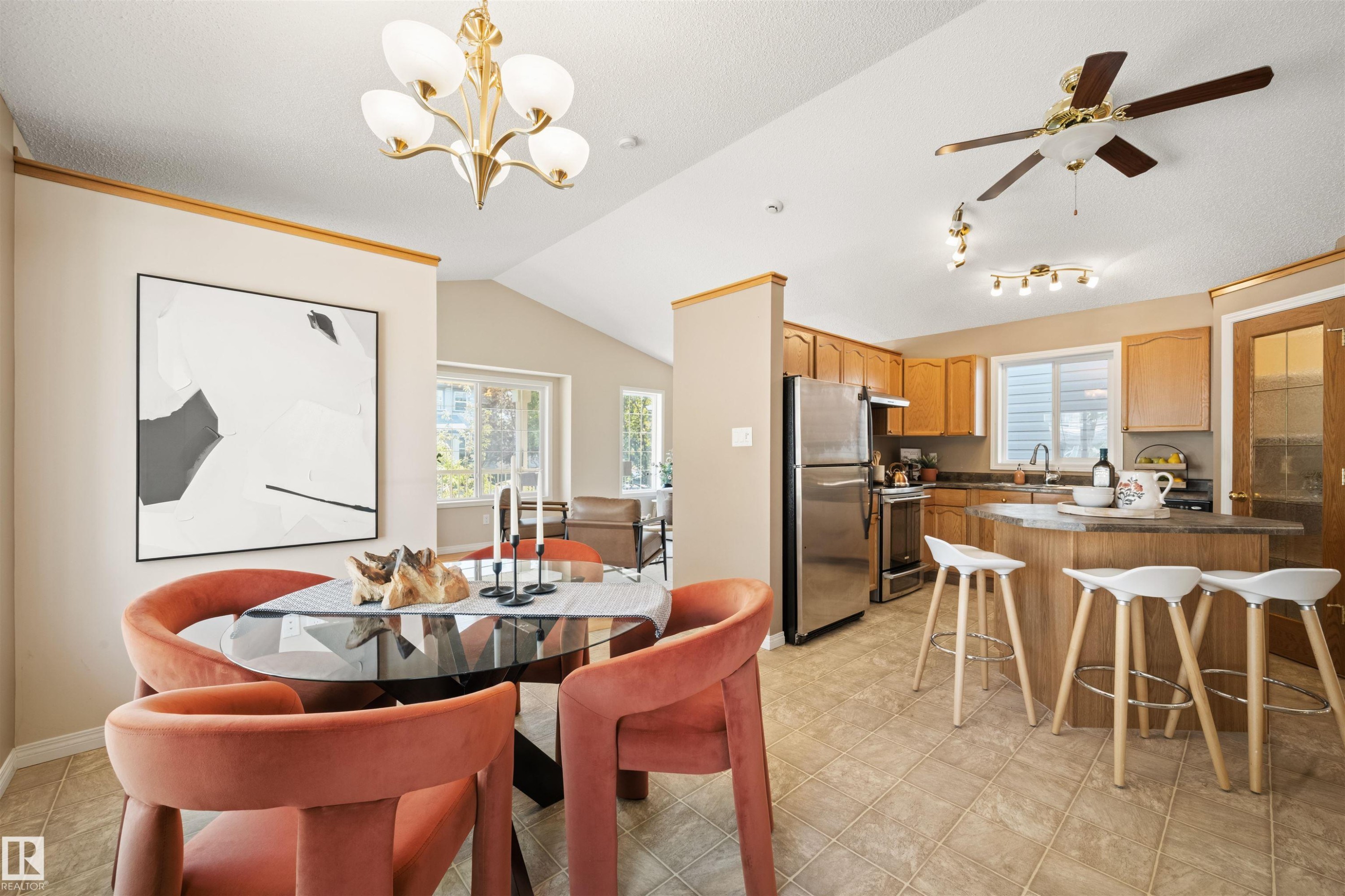 Open-concept kitchen and dining area featuring vaulted ceilings, tile flooring, stainless steel appliances, wood cabinetry, and an eat-at island - 7838 Schmid Place Nw, Edmonton, AB - Indoor Photo Showing Dining Room
