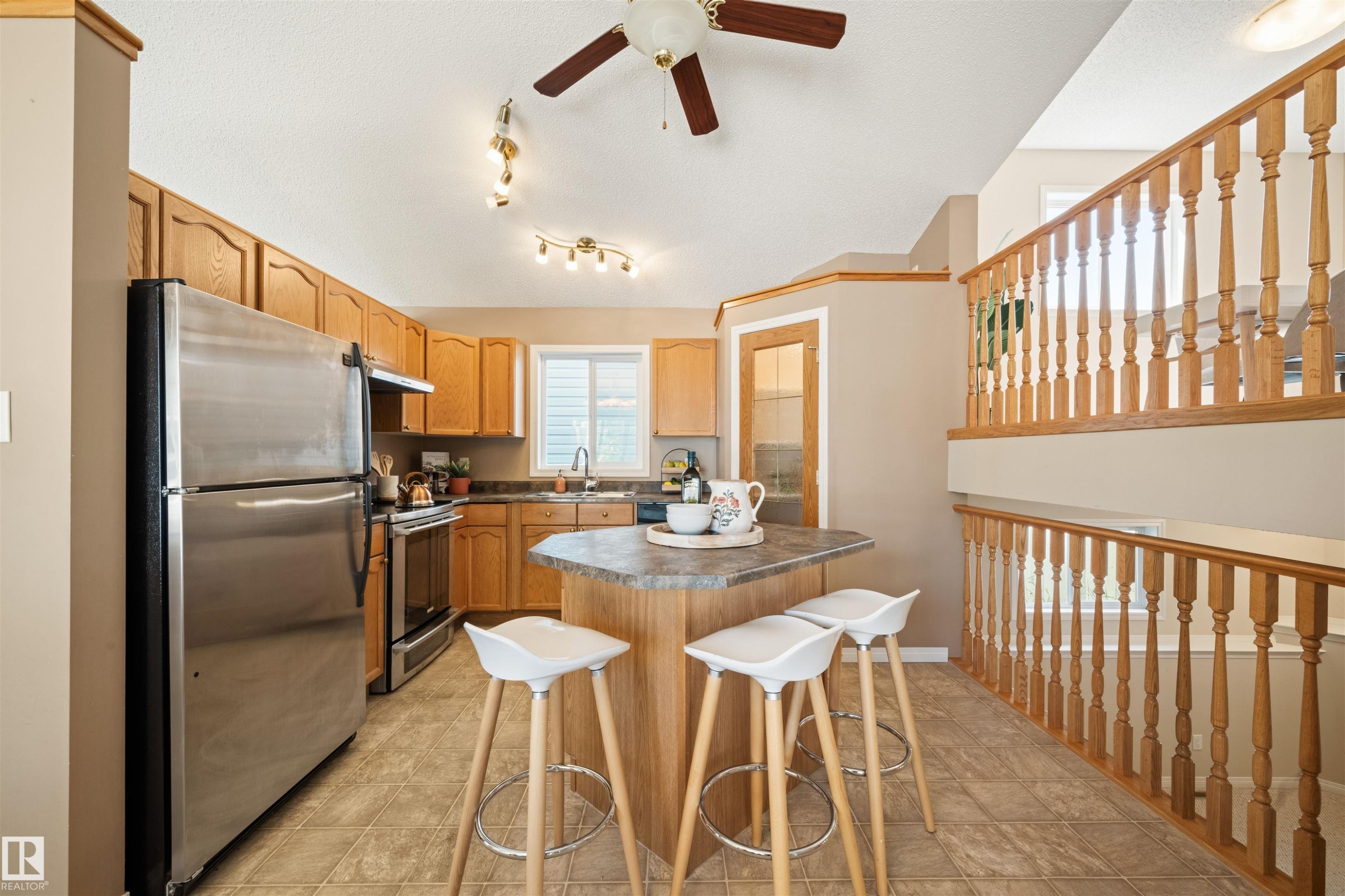 Kitchen featuring wood cabinetry, stainless steel appliances, a center island with countertop seating, and tile flooring - 7838 Schmid Place Nw, Edmonton, AB - Indoor