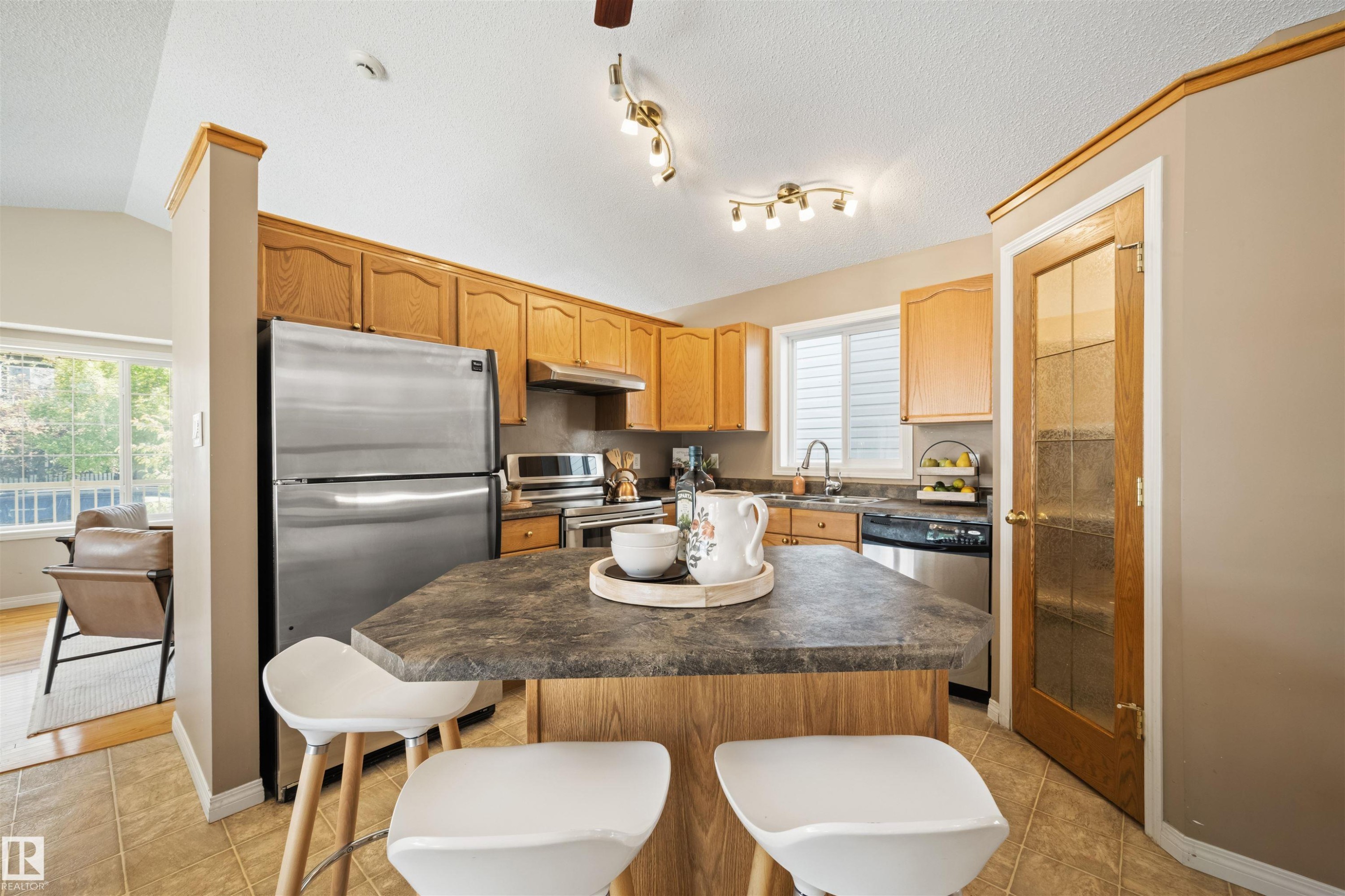Kitchen featuring a central island with countertop seating, wood cabinetry, and stainless steel appliances - 7838 Schmid Place Nw, Edmonton, AB - Indoor