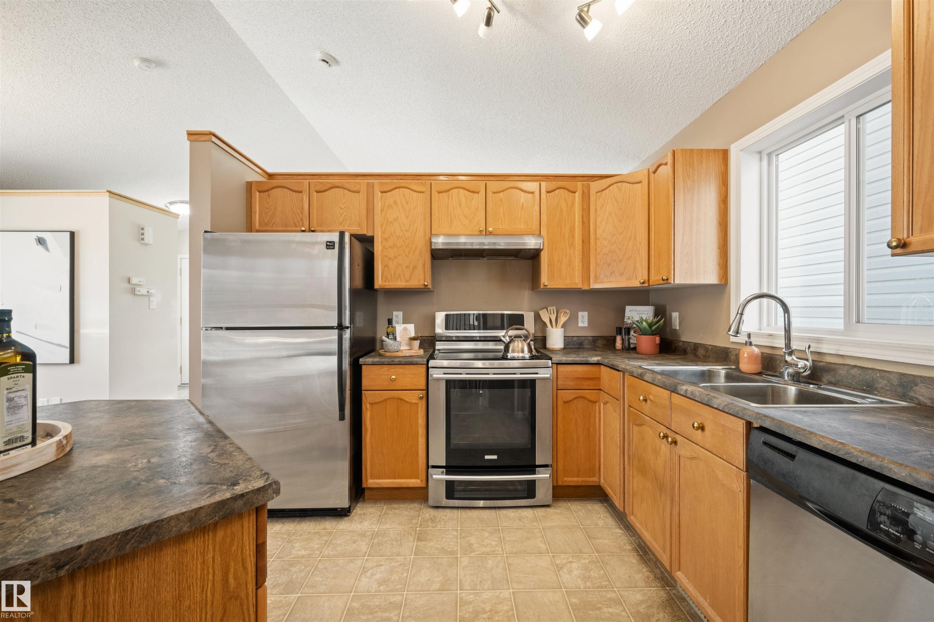 Kitchen featuring stainless steel appliances, wood cabinetry, laminate countertops, and a double basin sink - 7838 Schmid Place Nw, Edmonton, AB - Indoor Photo Showing Kitchen With Double Sink