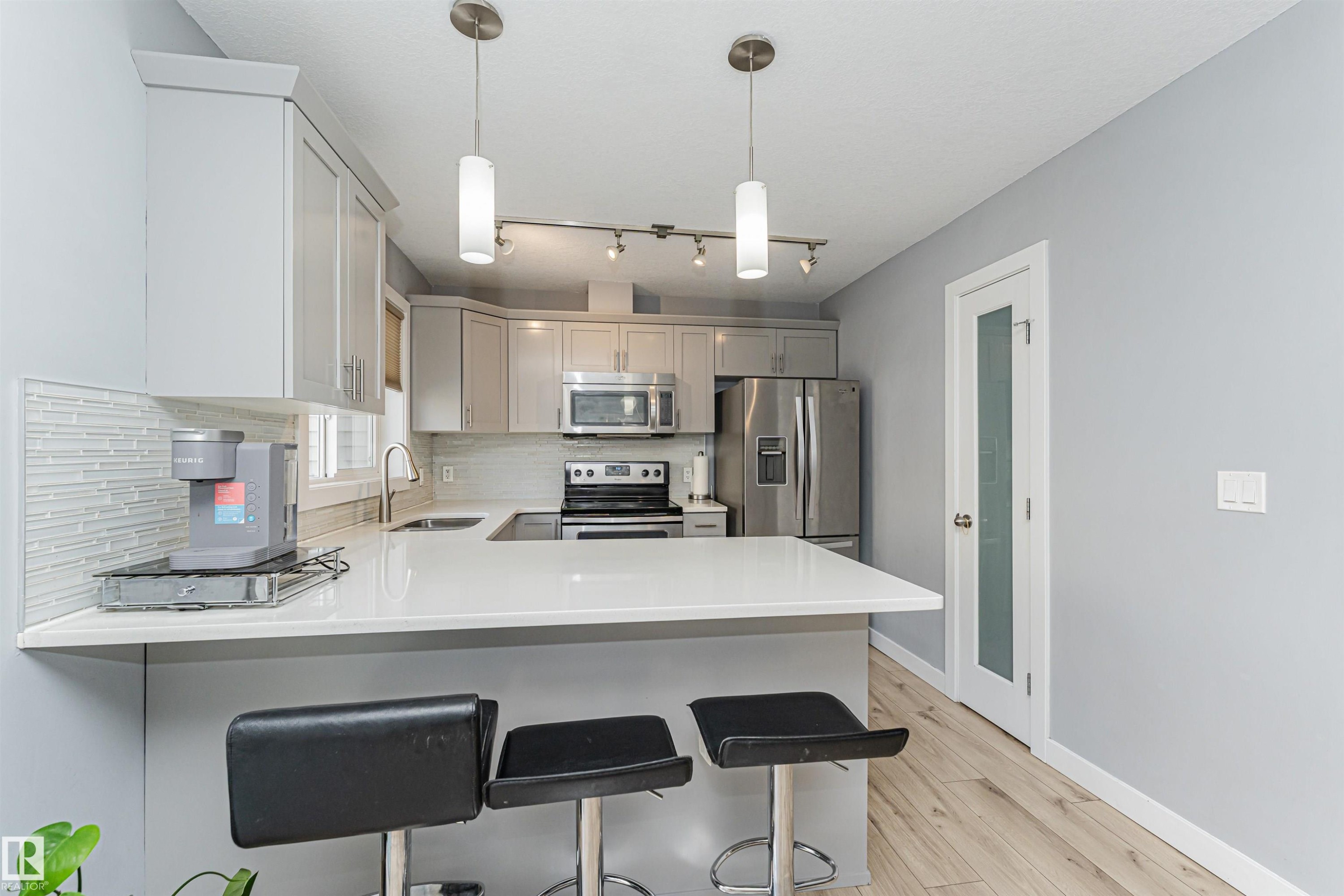 Contemporary kitchen featuring light gray cabinetry, stainless steel appliances, white countertops, and a white tile backsplash - 35 675 Albany Way, Edmonton, AB
