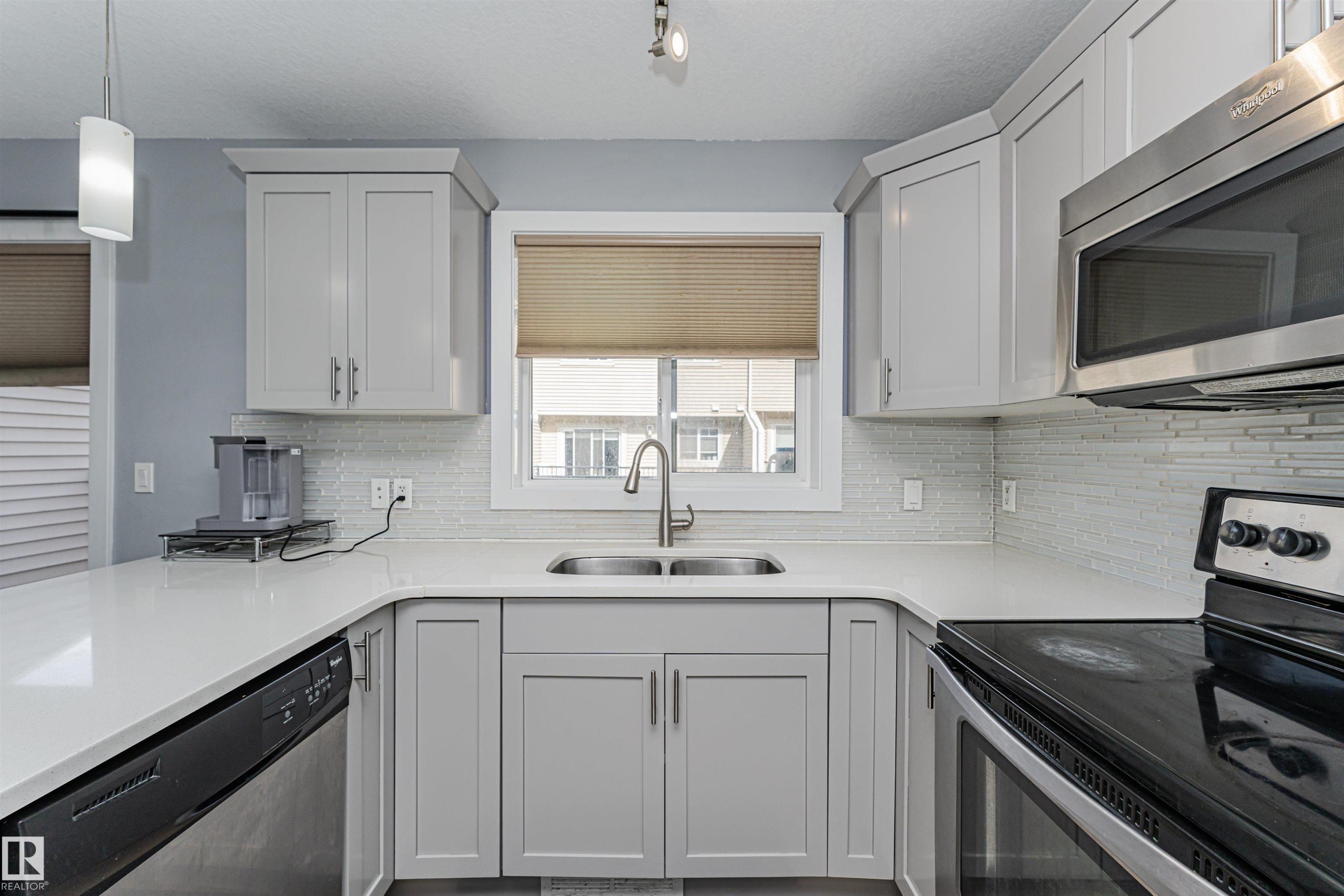 Kitchen featuring light gray cabinetry, white countertops, stainless steel appliances, a tile backsplash, and a double-basin sink - 35 675 Albany Way, Edmonton, AB