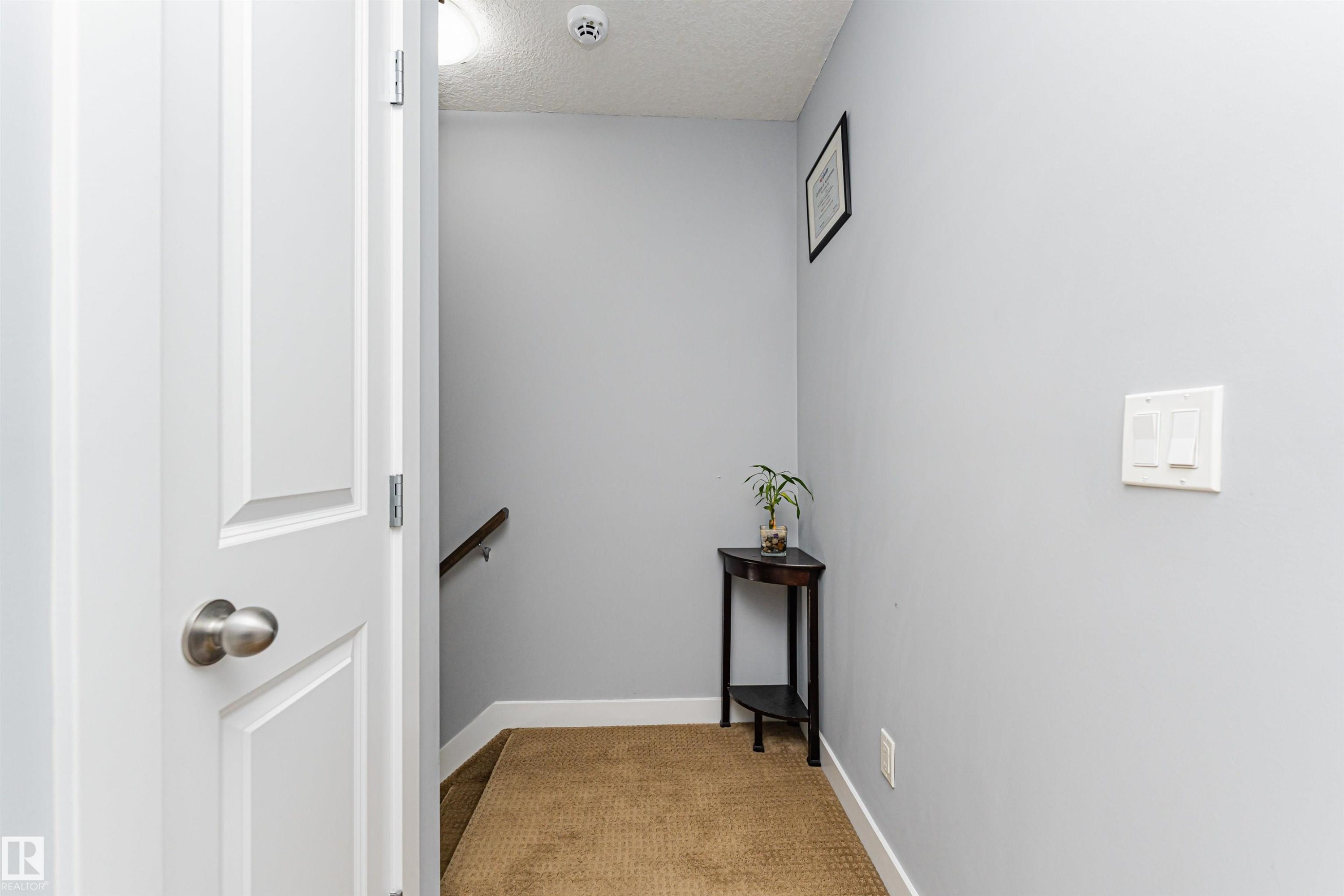Hallway featuring light gray walls, white trim, and a textured carpeted floor - 35 675 Albany Way, Edmonton, AB