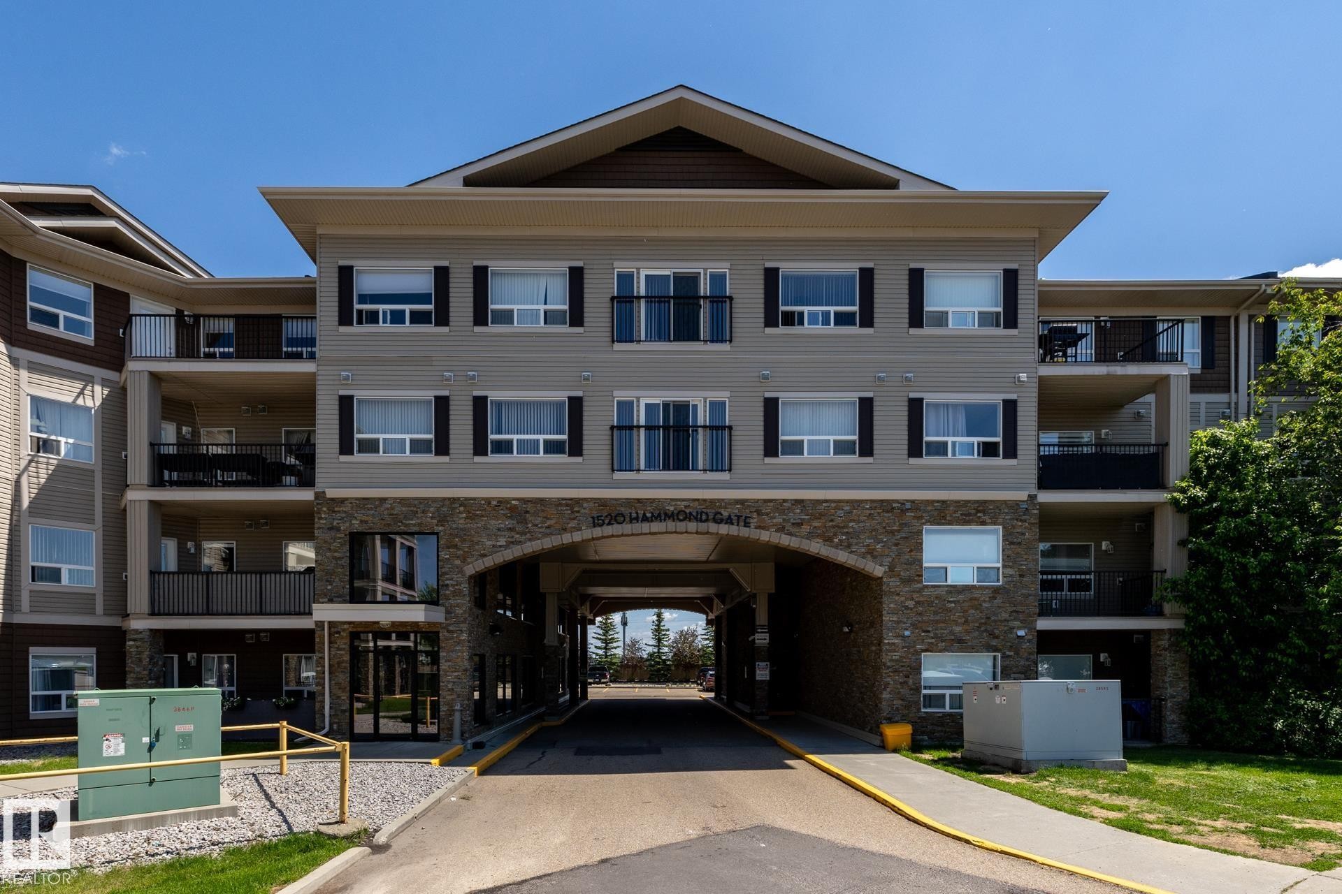 Multi-story building featuring a stone and siding exterior, multiple private balconies, and a central drive-through archway - 330 1520 Hammond Gate Gate, Edmonton, AB