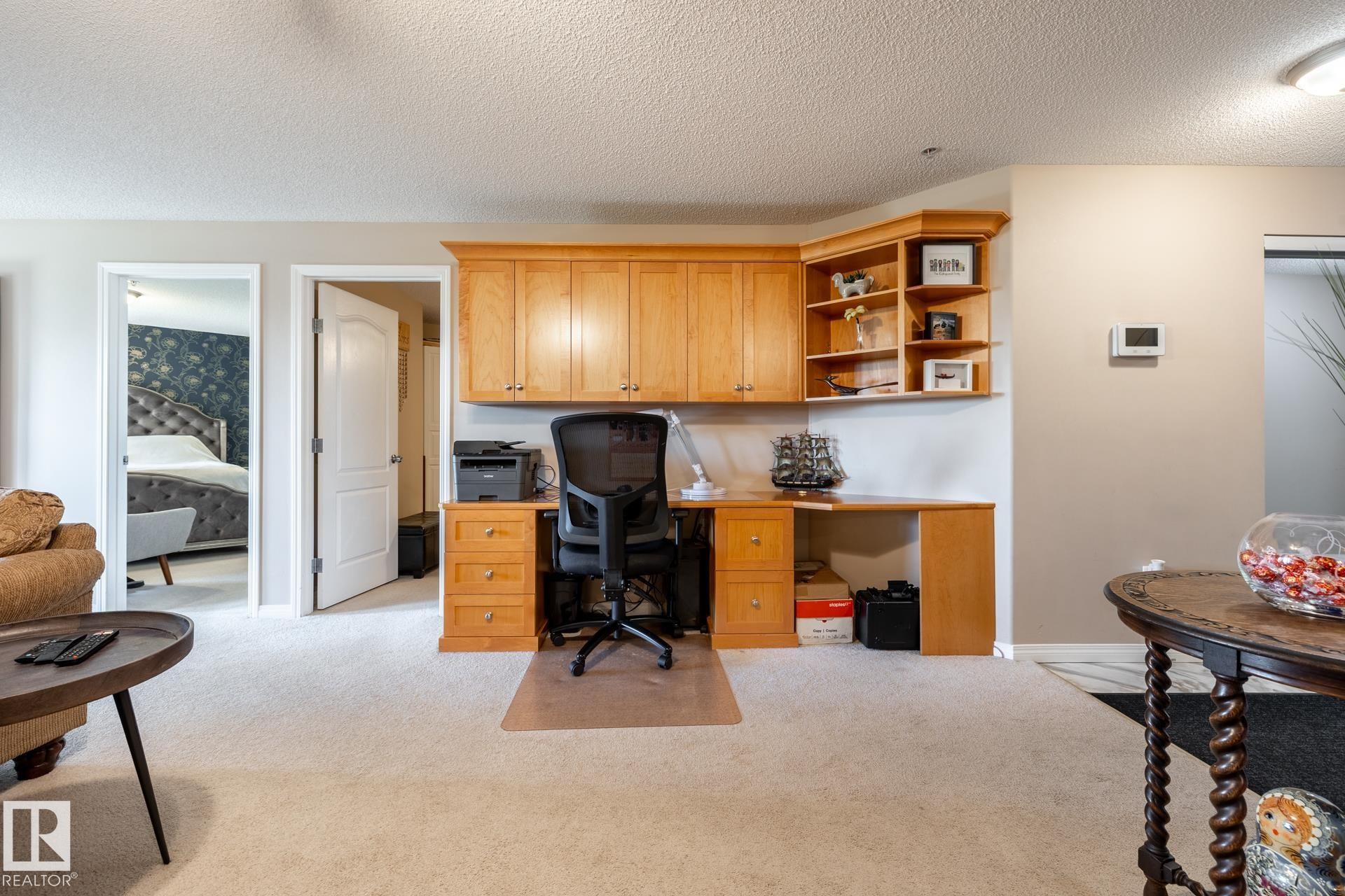 Integrated wood-finish desk with upper cabinetry and shelving, set against neutral wall tones and textured carpeting - 330 1520 Hammond Gate Gate, Edmonton, AB