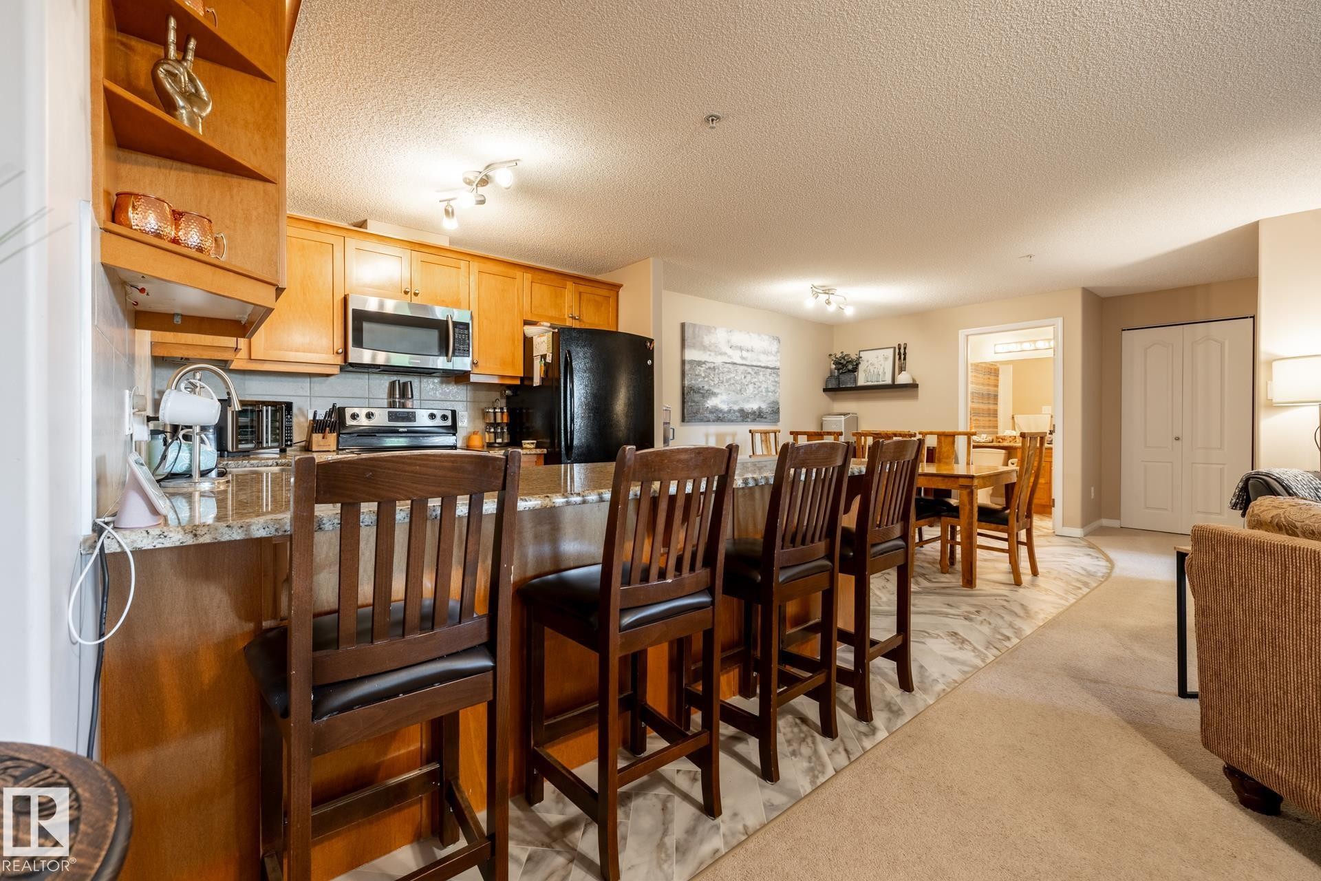 Kitchen featuring a granite-style breakfast bar, light wood-finish cabinetry, stainless steel microwave, and tile backsplash - 330 1520 Hammond Gate Gate, Edmonton, AB
