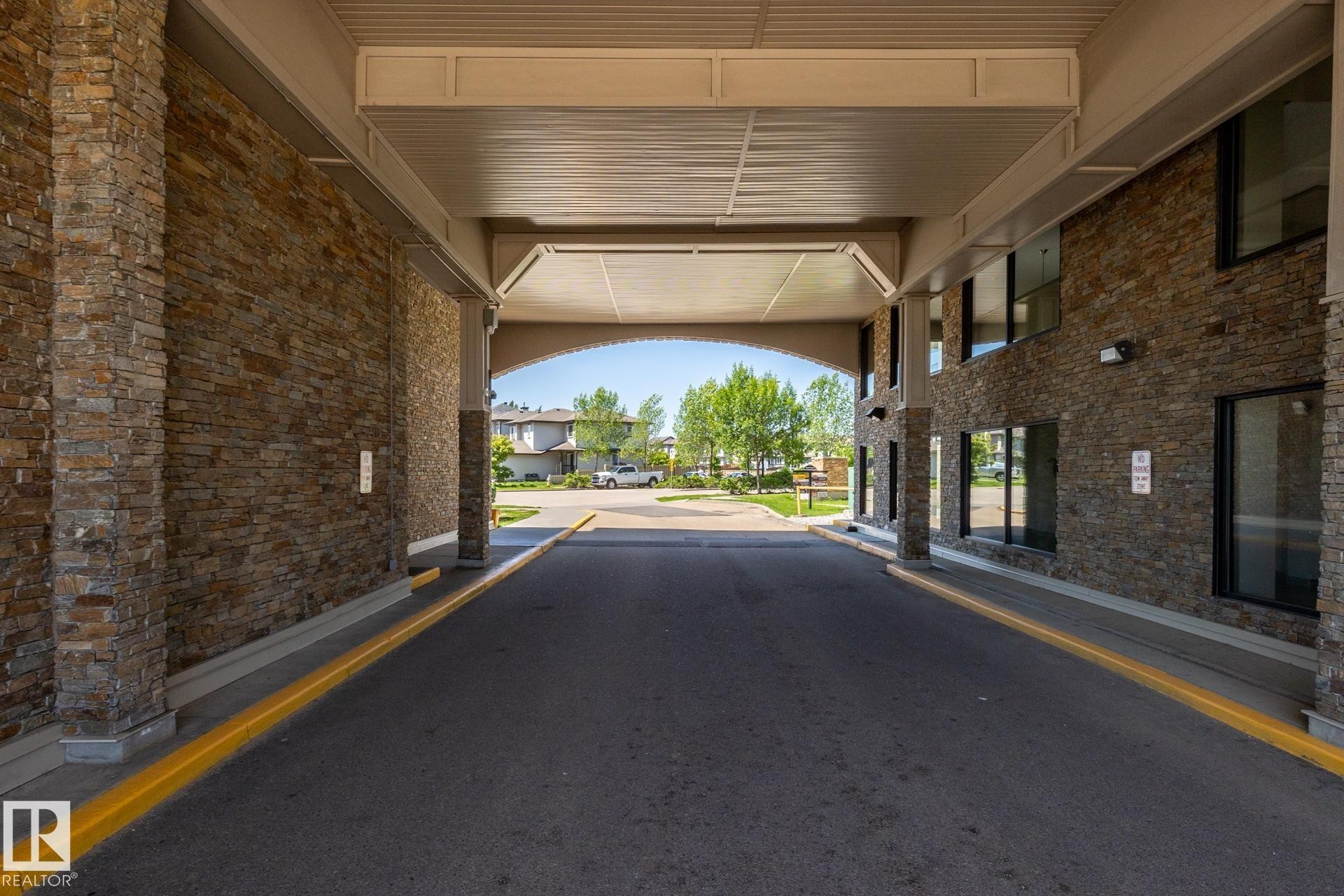 Covered entry drive with stone veneer columns and exterior walls, under a light-colored soffit - 330 1520 Hammond Gate Gate, Edmonton, AB