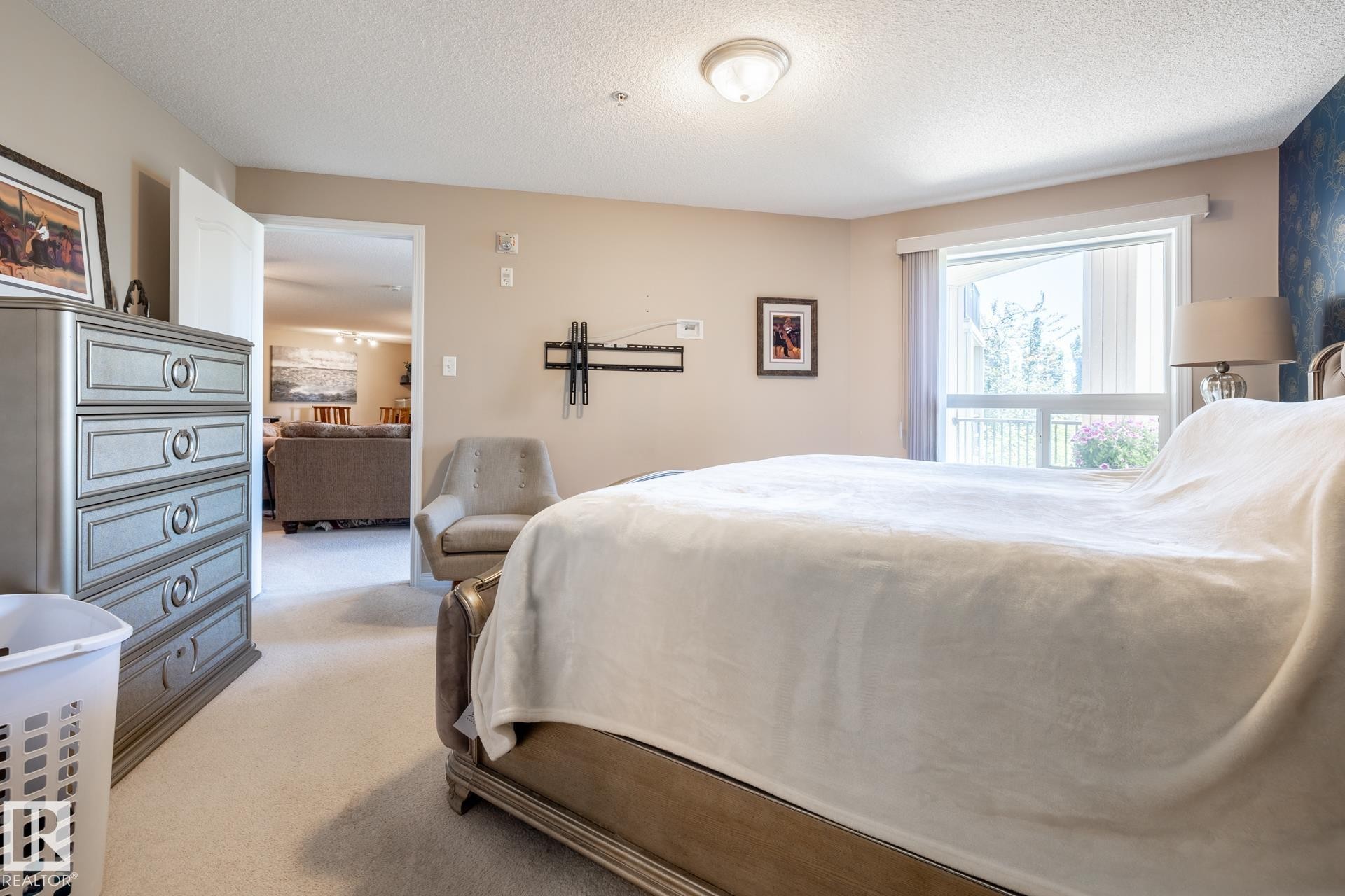 Carpeted bedroom with a large window, a ceiling-mounted light fixture, and a wall-mounted bracket - 330 1520 Hammond Gate Gate, Edmonton, AB