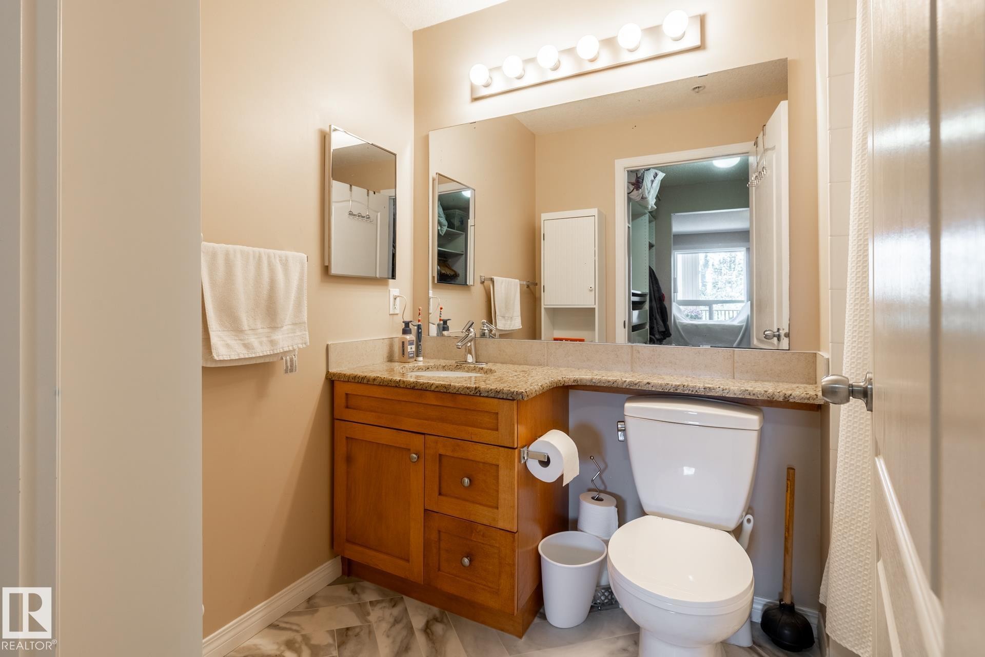 Bathroom vanity featuring wood cabinetry, a light-toned countertop, and a large wall-mounted mirror with overhead bar lighting - 330 1520 Hammond Gate Gate, Edmonton, AB