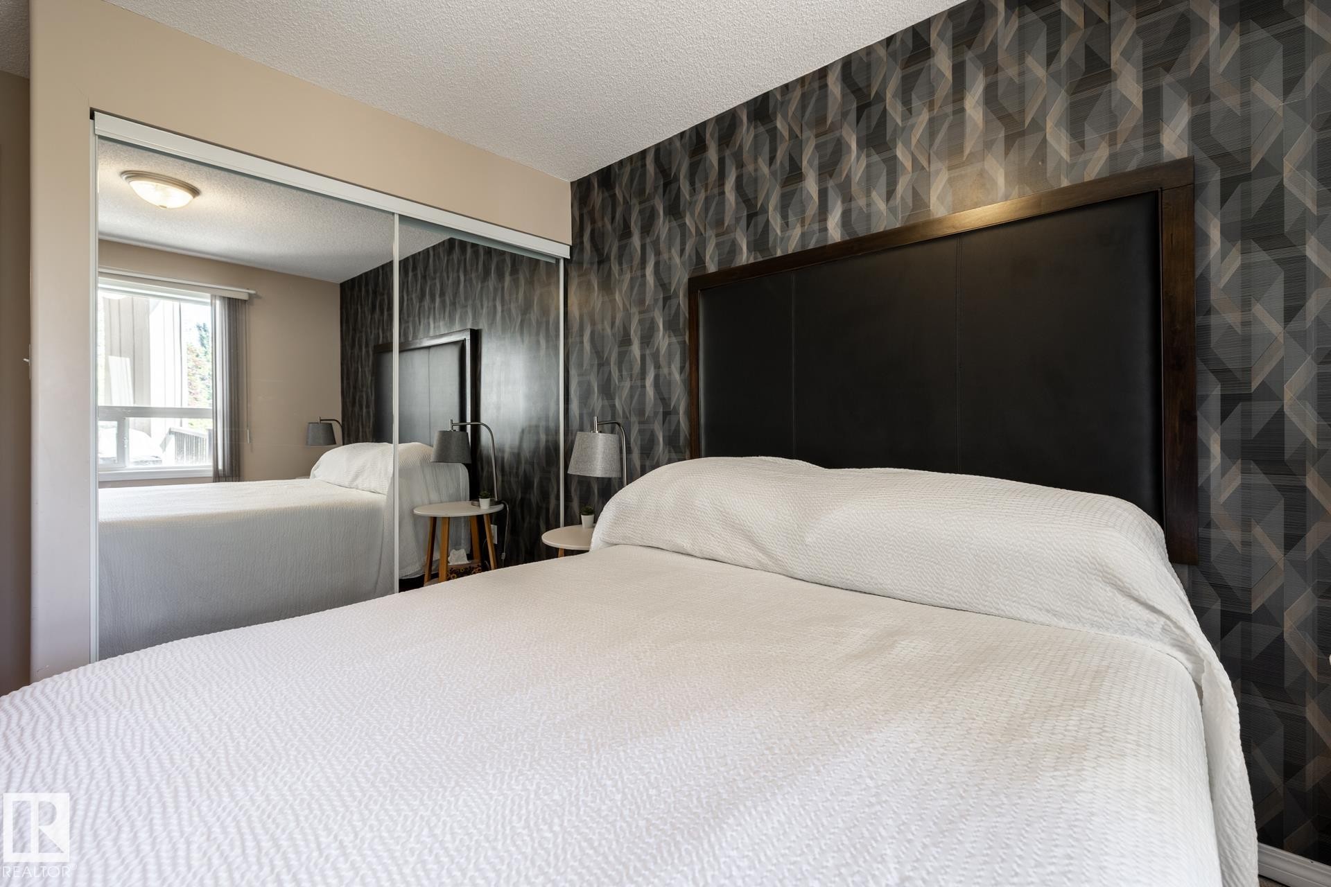 Mirrored sliding closet doors with an overhead light fixture, a window with blinds, and a feature wall with geometric pattern wallpaper - 330 1520 Hammond Gate Gate, Edmonton, AB