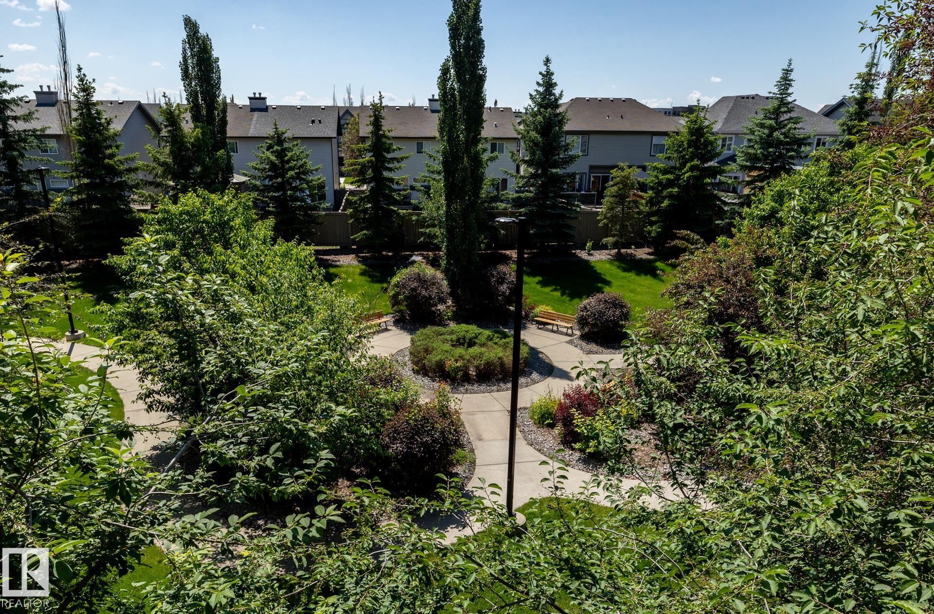 Landscaped communal green space featuring a winding paved pathway, mature trees, manicured lawns, and built-in benches - 330 1520 Hammond Gate Gate, Edmonton, AB