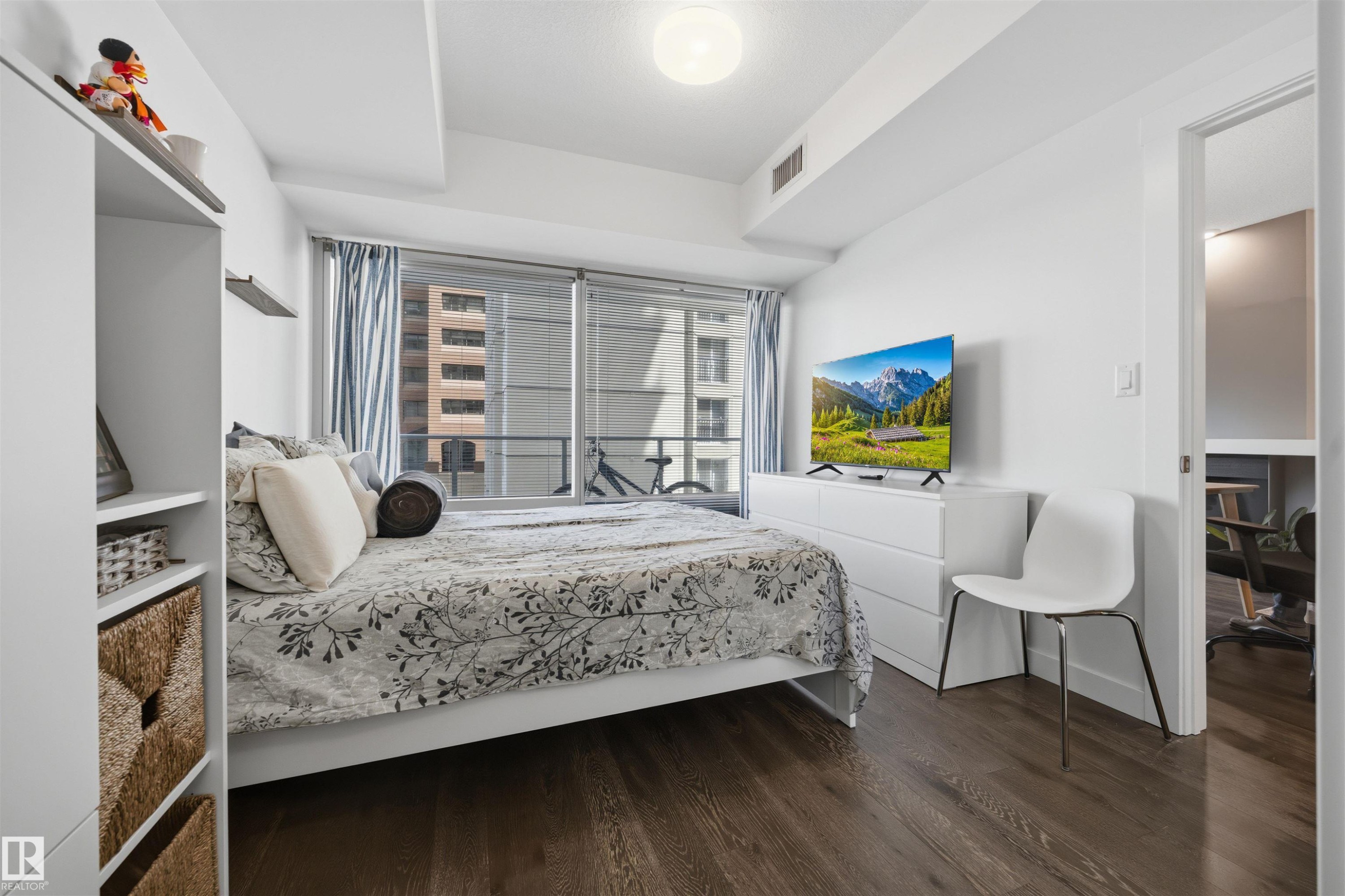 Wood-finish flooring throughout, complemented by a full-wall window with vertical blinds - #802 9720 106 St Nw, Edmonton, AB - Indoor Photo Showing Bedroom