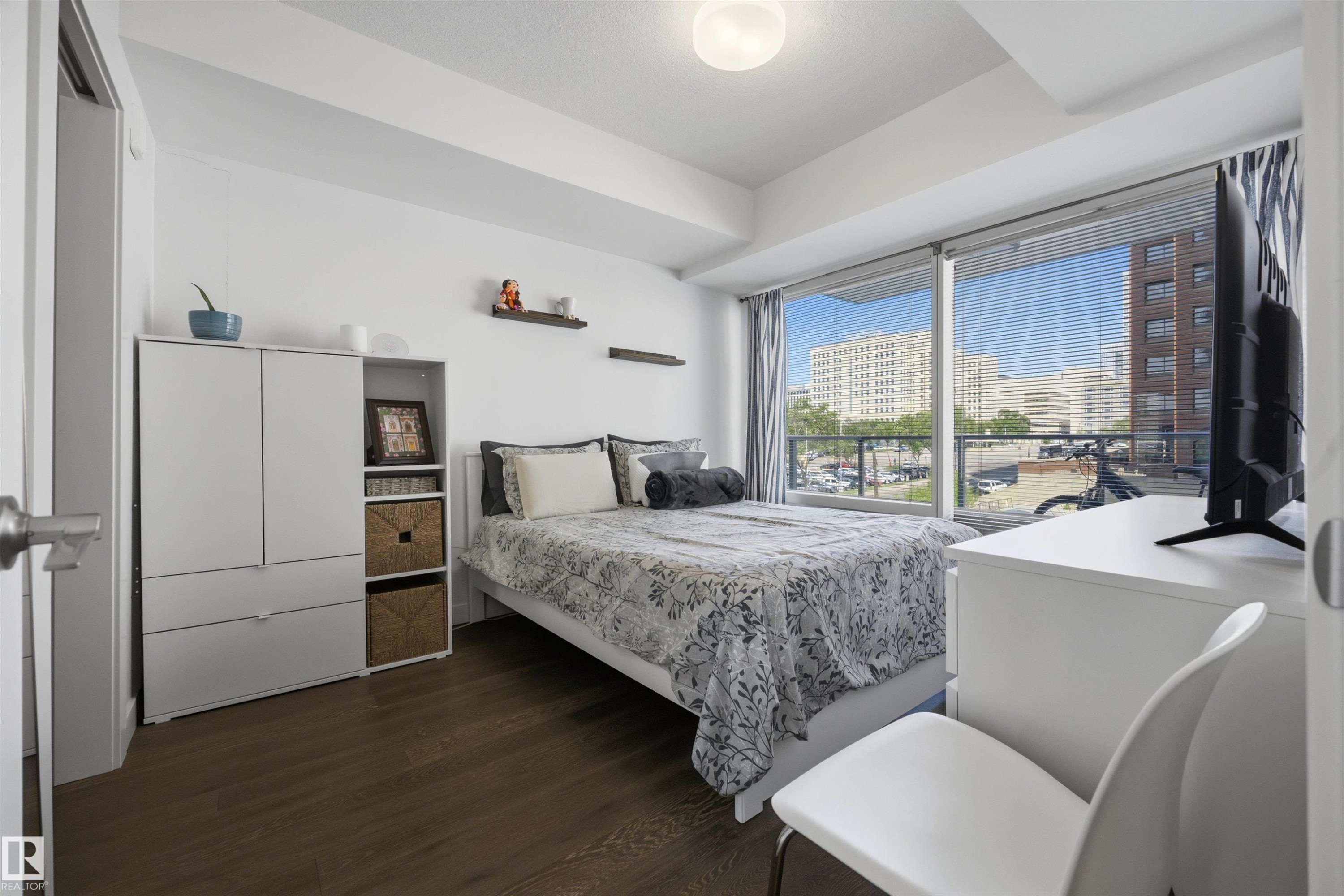 Bedroom featuring expansive floor-to-ceiling windows, wood-finish flooring, and a contemporary ceiling light fixture - #802 9720 106 St Nw, Edmonton, AB - Indoor Photo Showing Bedroom