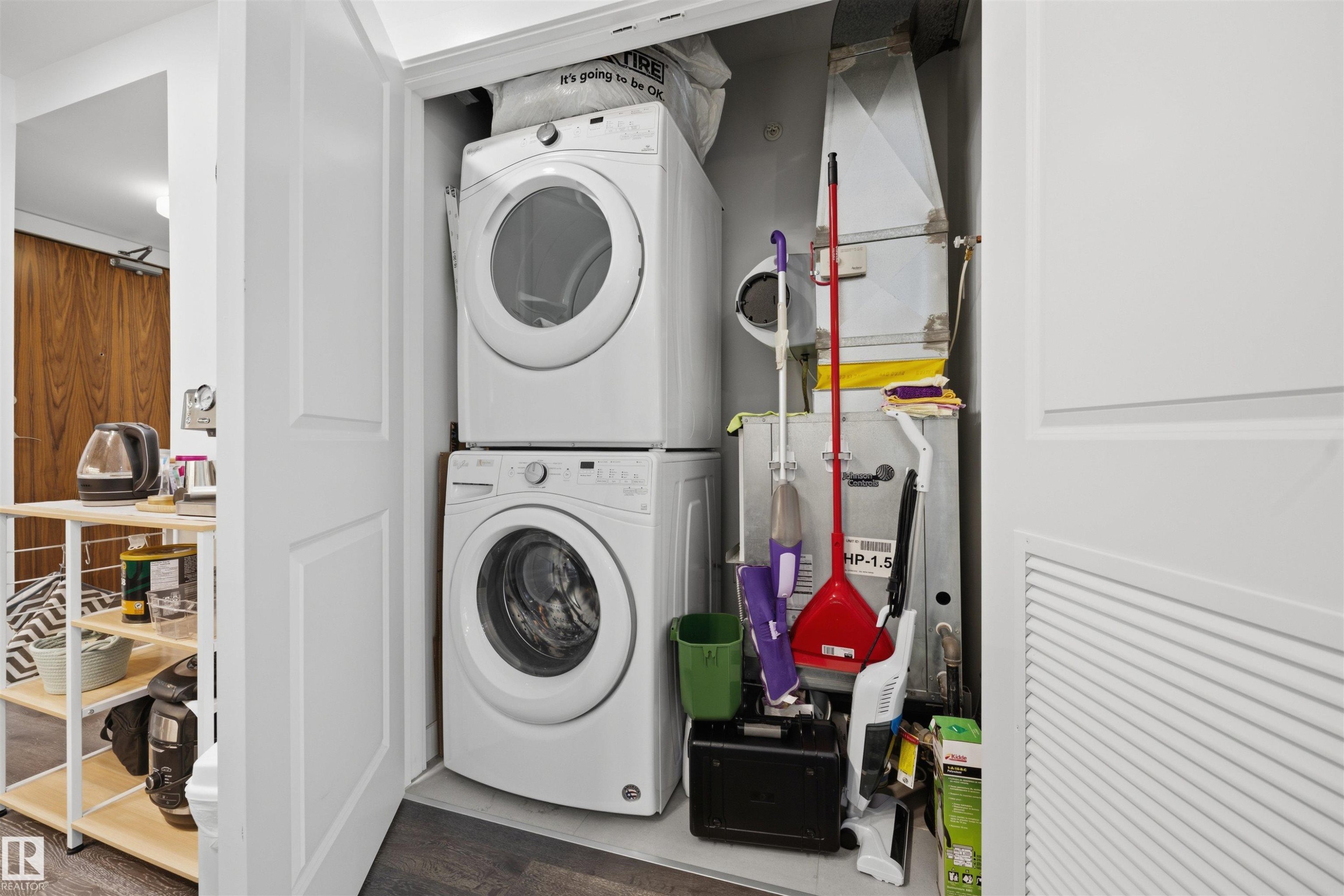 Dedicated laundry closet featuring a stacked washer and dryer unit, wood-finish flooring, and white paneled doors - #802 9720 106 St Nw, Edmonton, AB - Indoor Photo Showing Laundry Room