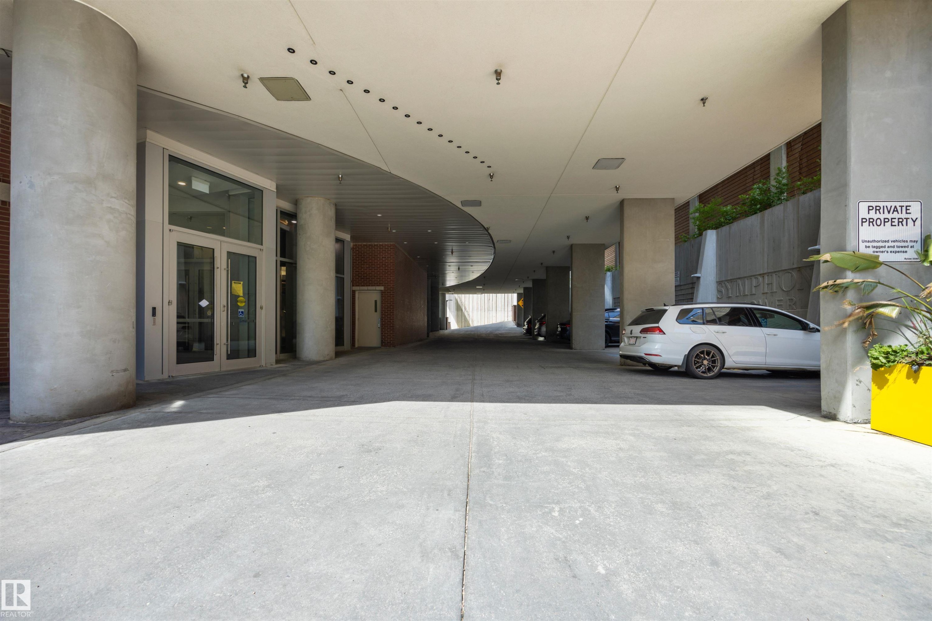 Covered concrete driveway providing access to the building entrance with glass doors, and a parking area with concrete pillars Visitor Parking - #802 9720 106 St Nw, Edmonton, AB - Photo Showing Garage