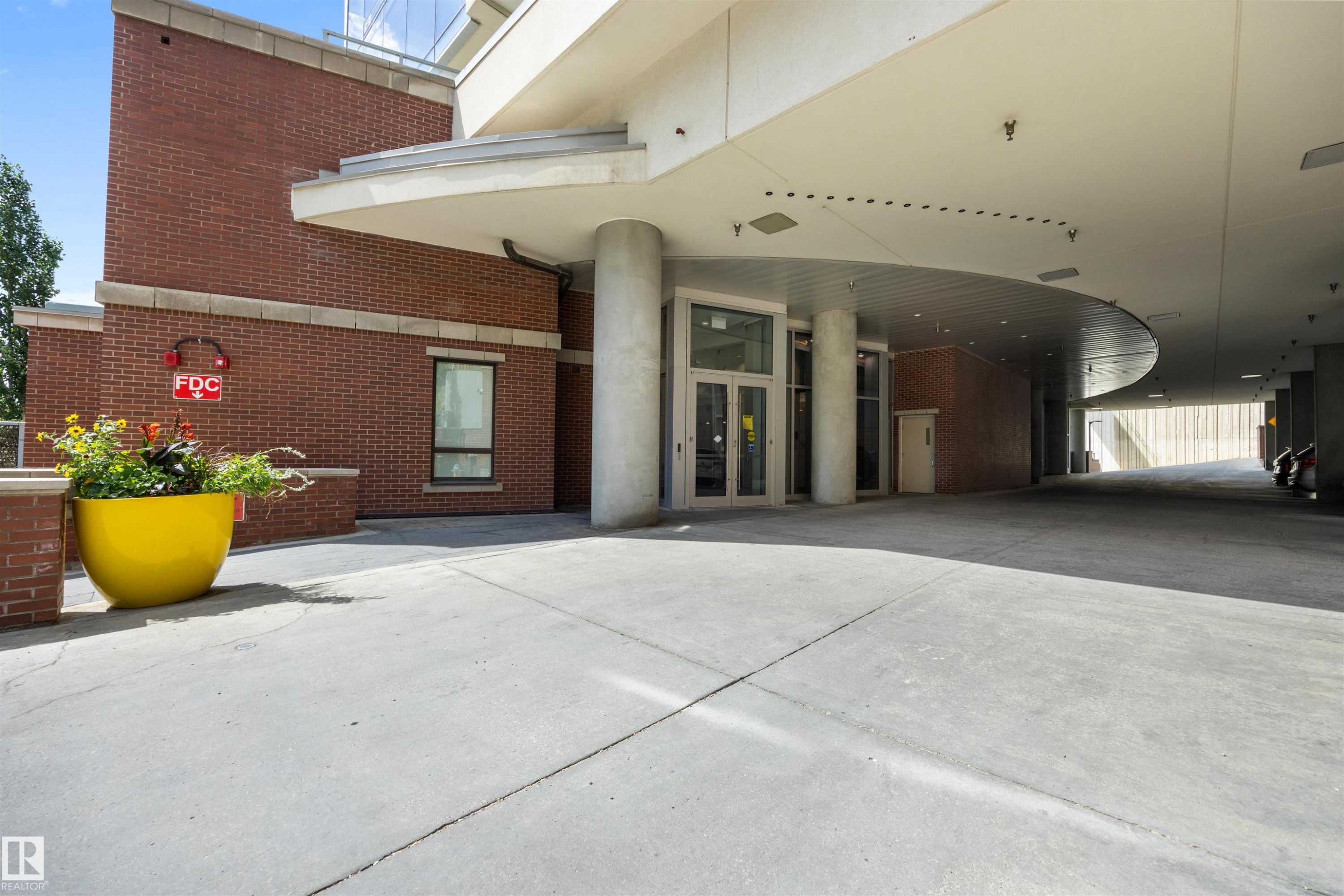 Building entrance featuring brick facade and a wide concrete approach - #802 9720 106 St Nw, Edmonton, AB - Outdoor With Exterior