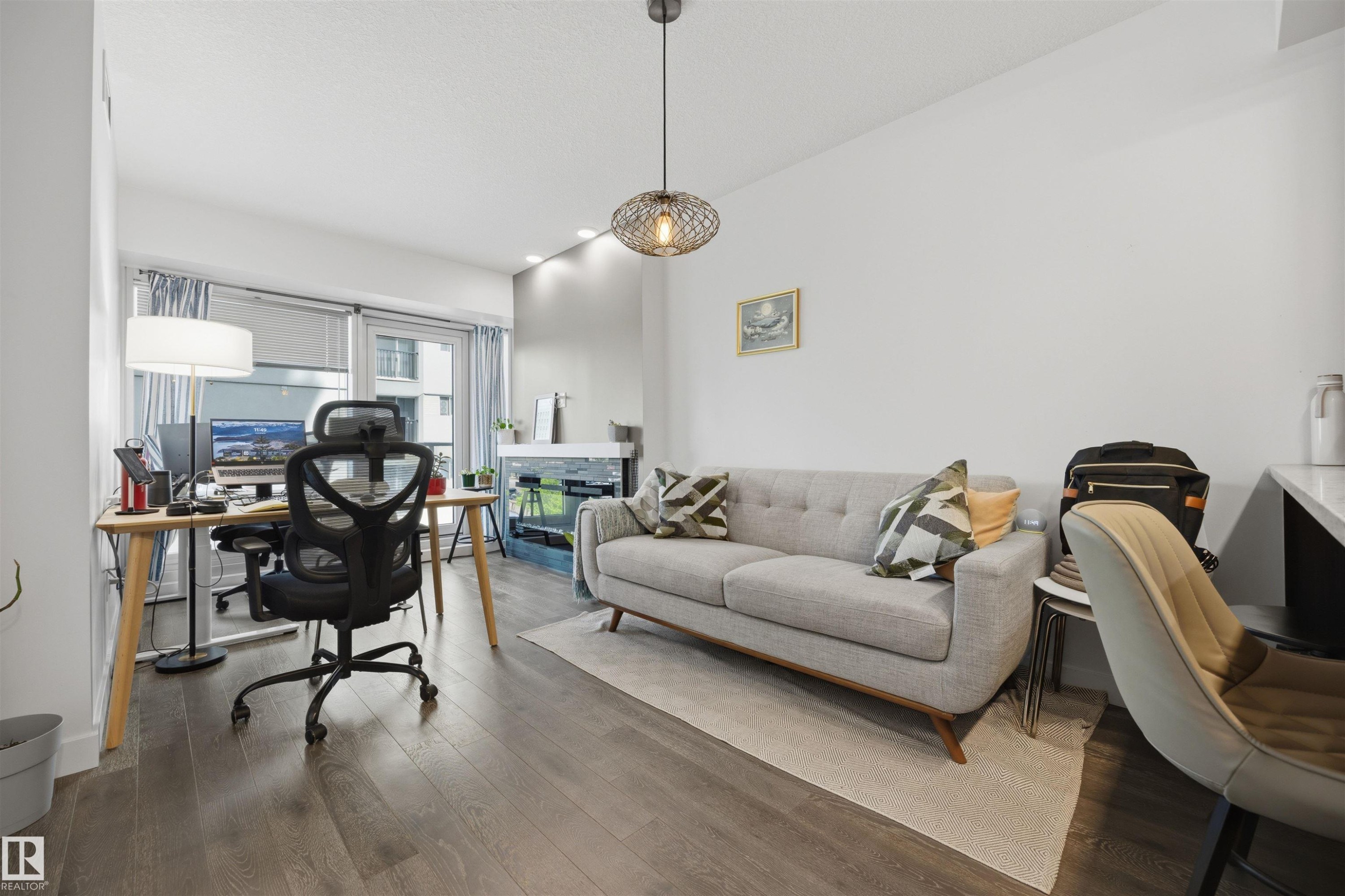 Spacious room featuring wood-finish flooring, a contemporary ceiling light fixture, and recessed lighting - #802 9720 106 St Nw, Edmonton, AB - Indoor