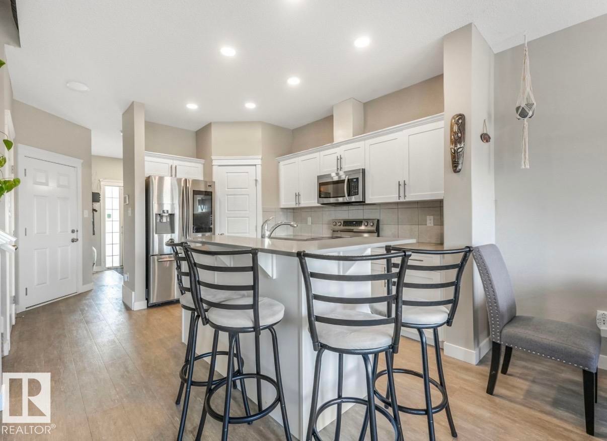 Kitchen featuring white cabinetry, stainless steel appliances, a light-toned backsplash, recessed lighting, and an island with counter seating - 17171 38 Street, Edmonton, AB